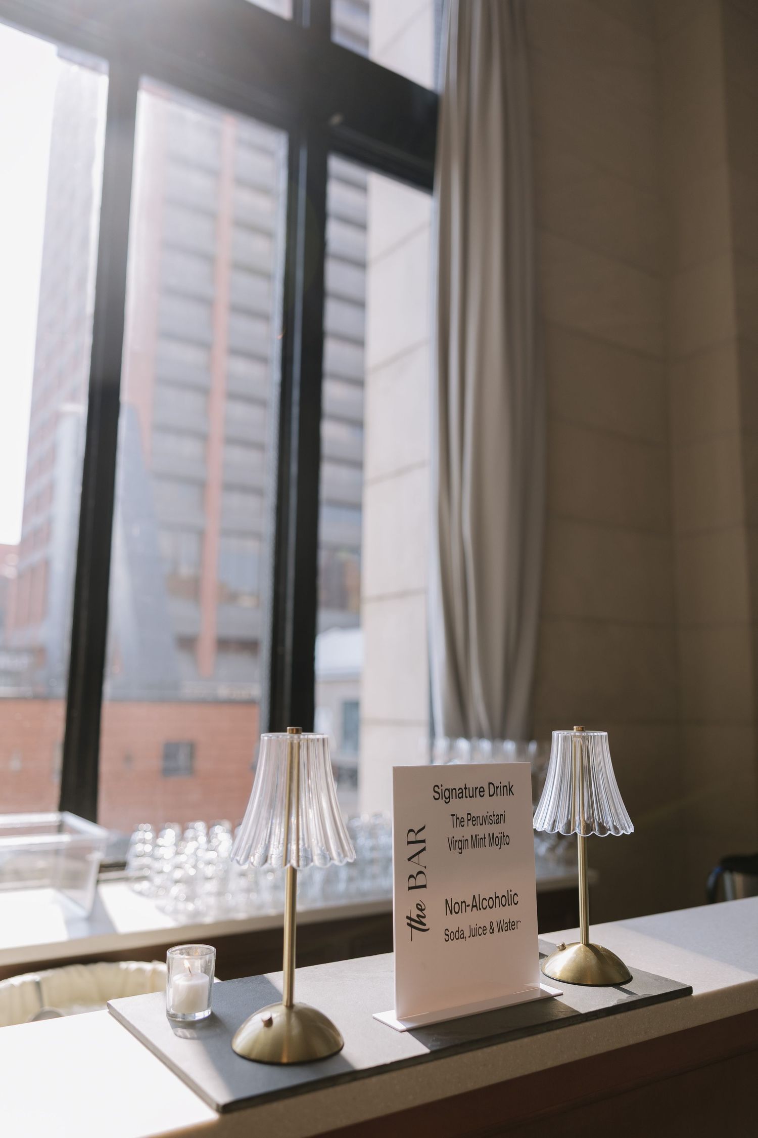 Two small table lamps and signature cards sit on a windowsill overlooking a city building view.