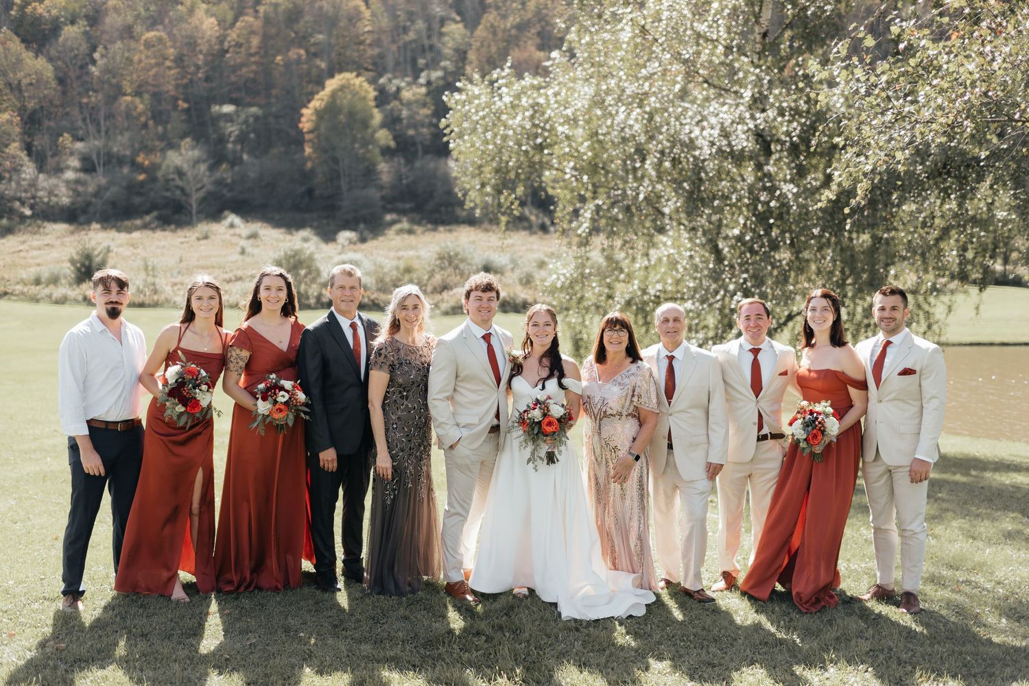 Wedding party in burgundy and neutral colors poses together in an outdoor field on a sunny day.