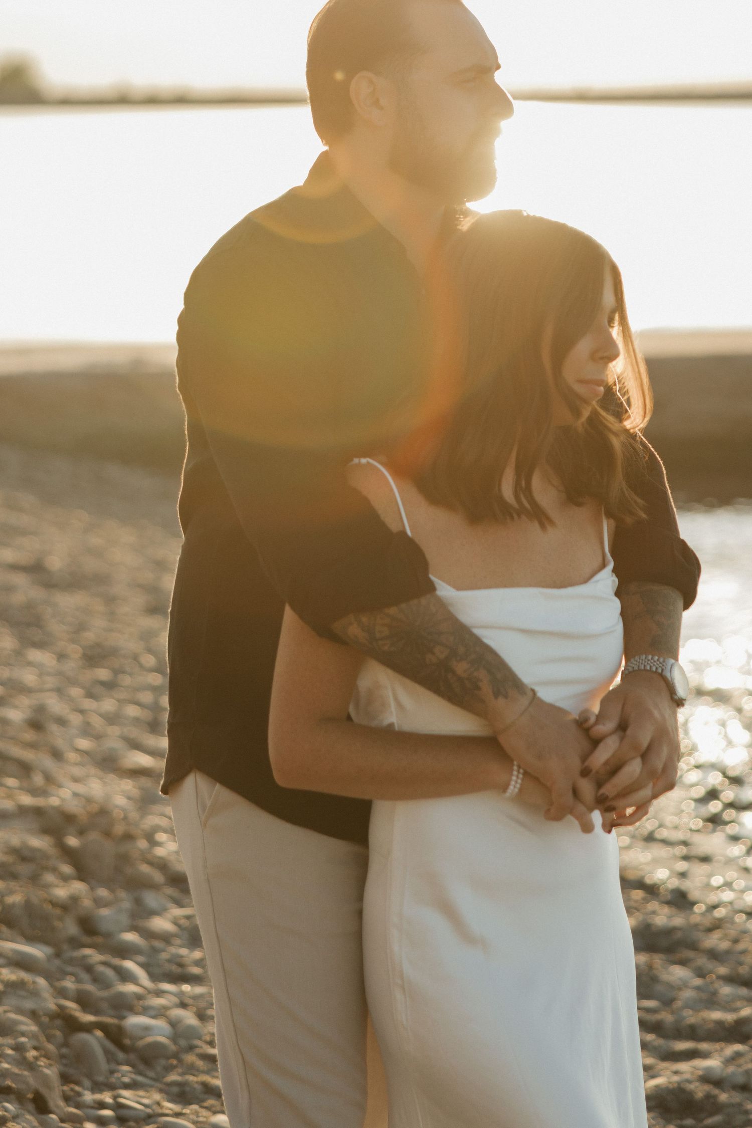 A couple embraces on a beach at sunset with warm golden light illuminating their silhouettes.