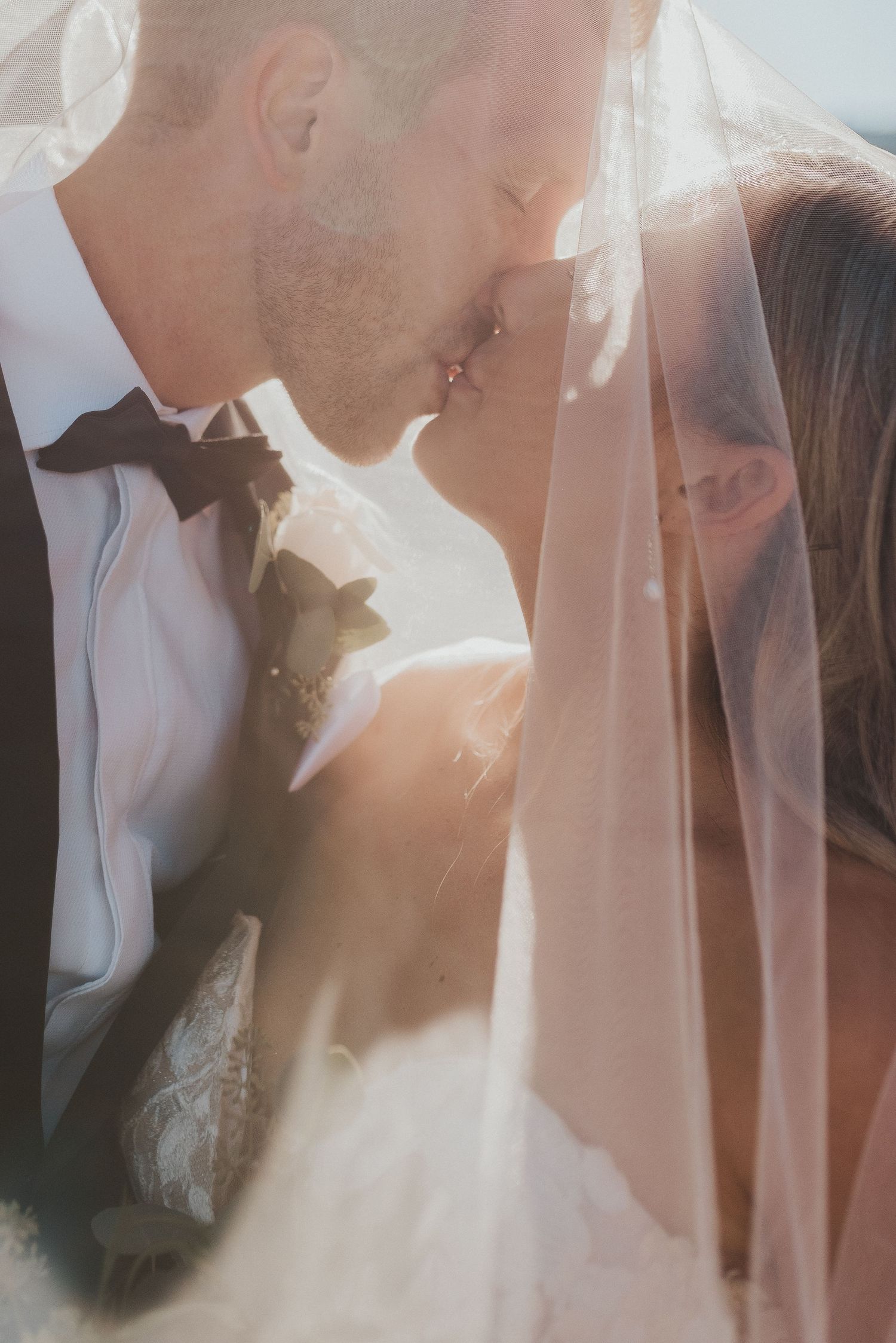 Romantic wedding moment captured through delicate veil with sunlight streaming through creating ethereal glow.