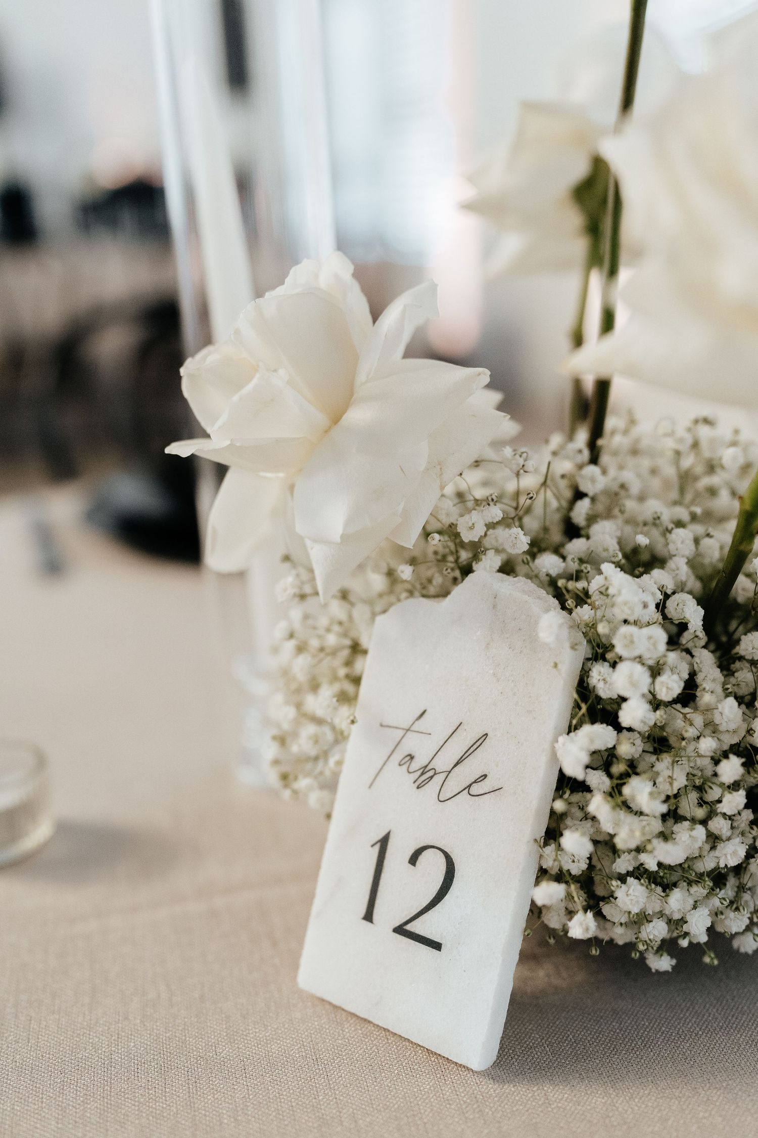 Elegant white floral wedding table numbers with baby's breath and roses arranged on linen tablecloths.