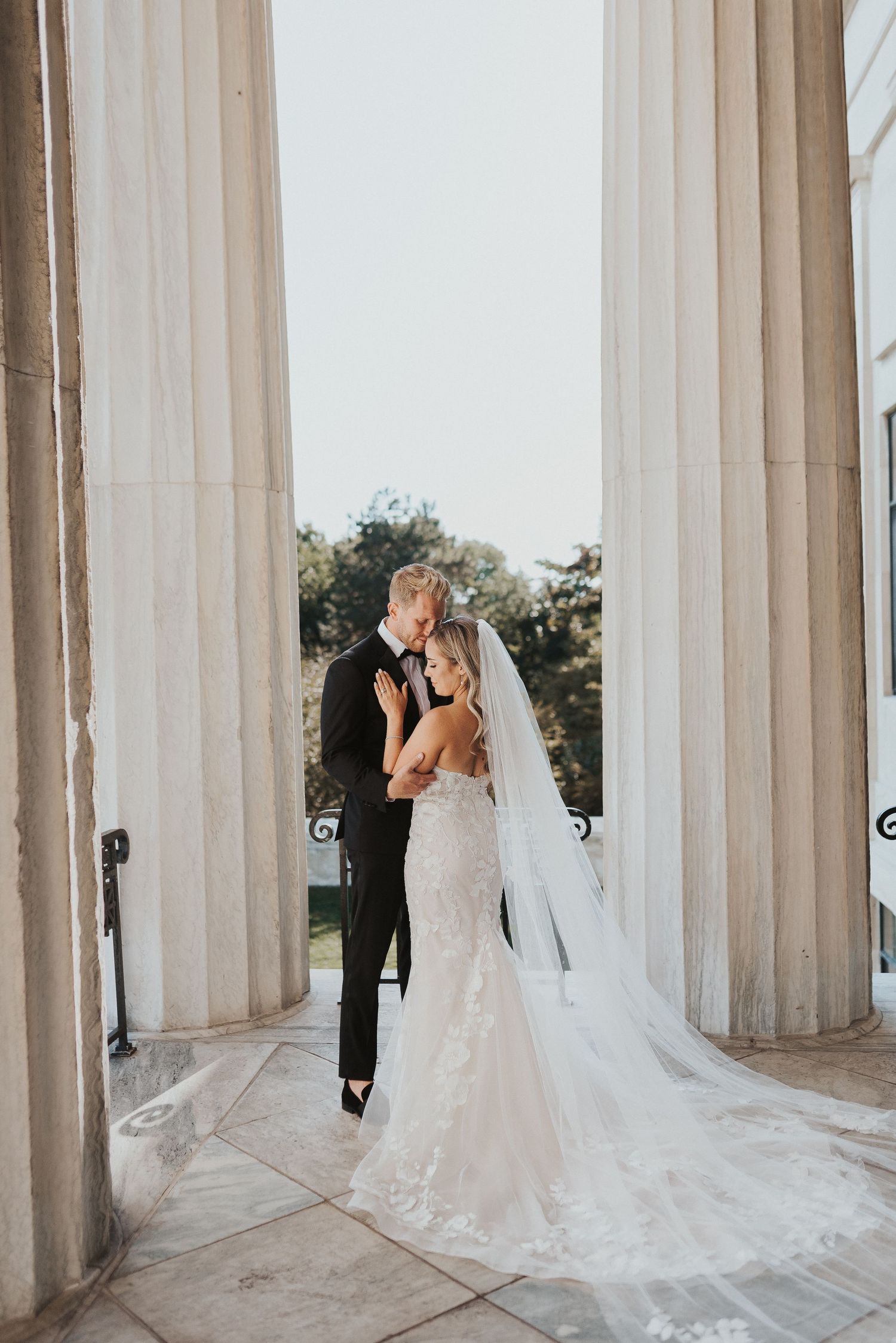 A romantic wedding photo shoot among elegant white marble columns with flowing veils creating ethereal silhouettes.