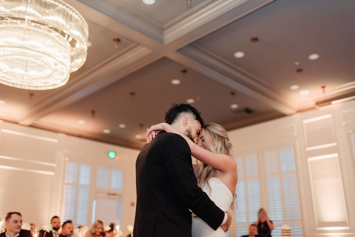 Wedding guests dance and celebrate together on an elegant ballroom dance floor under crystal chandeliers.
