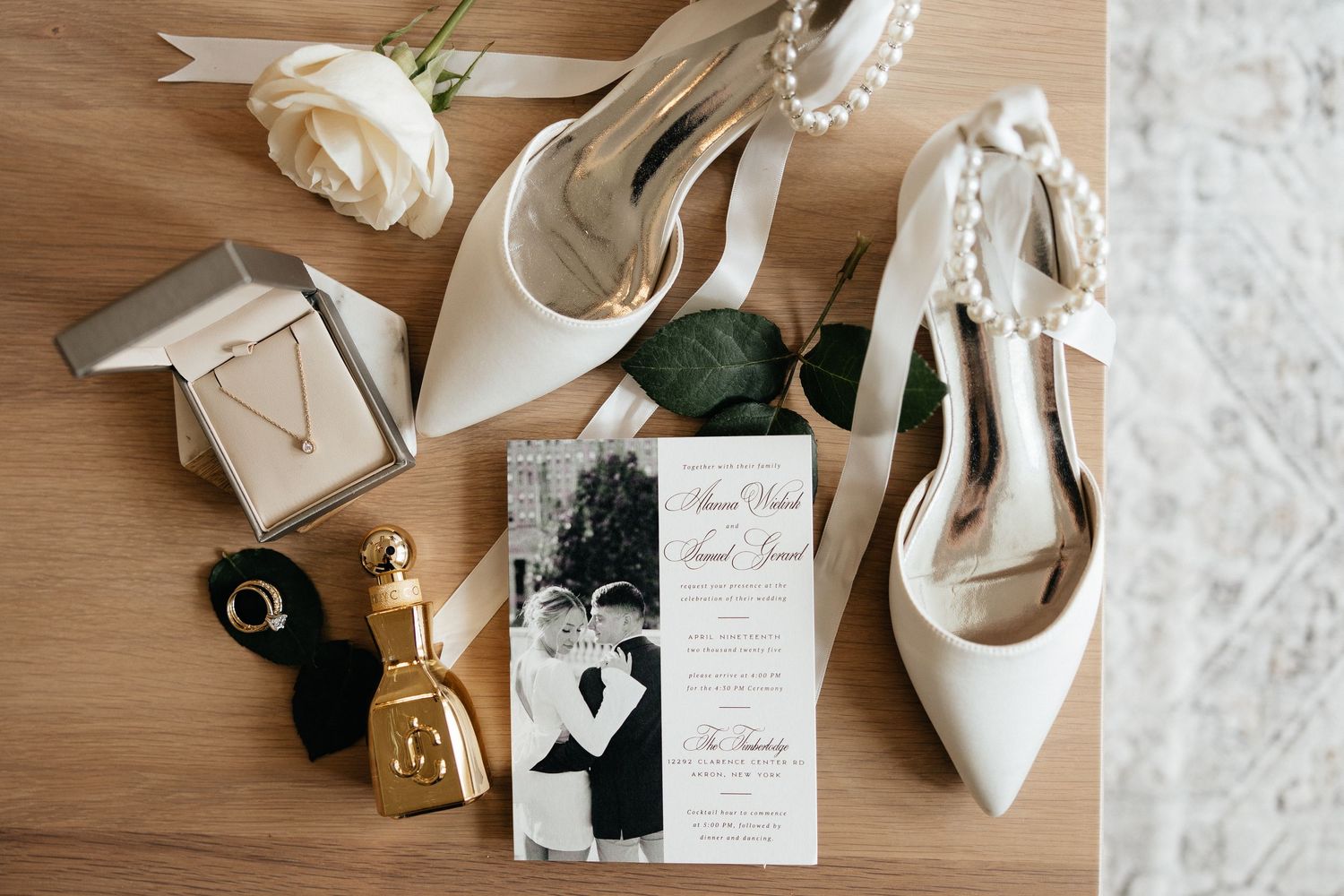 Elegant wedding details including white shoes, invitations, and accessories arranged on a light wooden surface.
