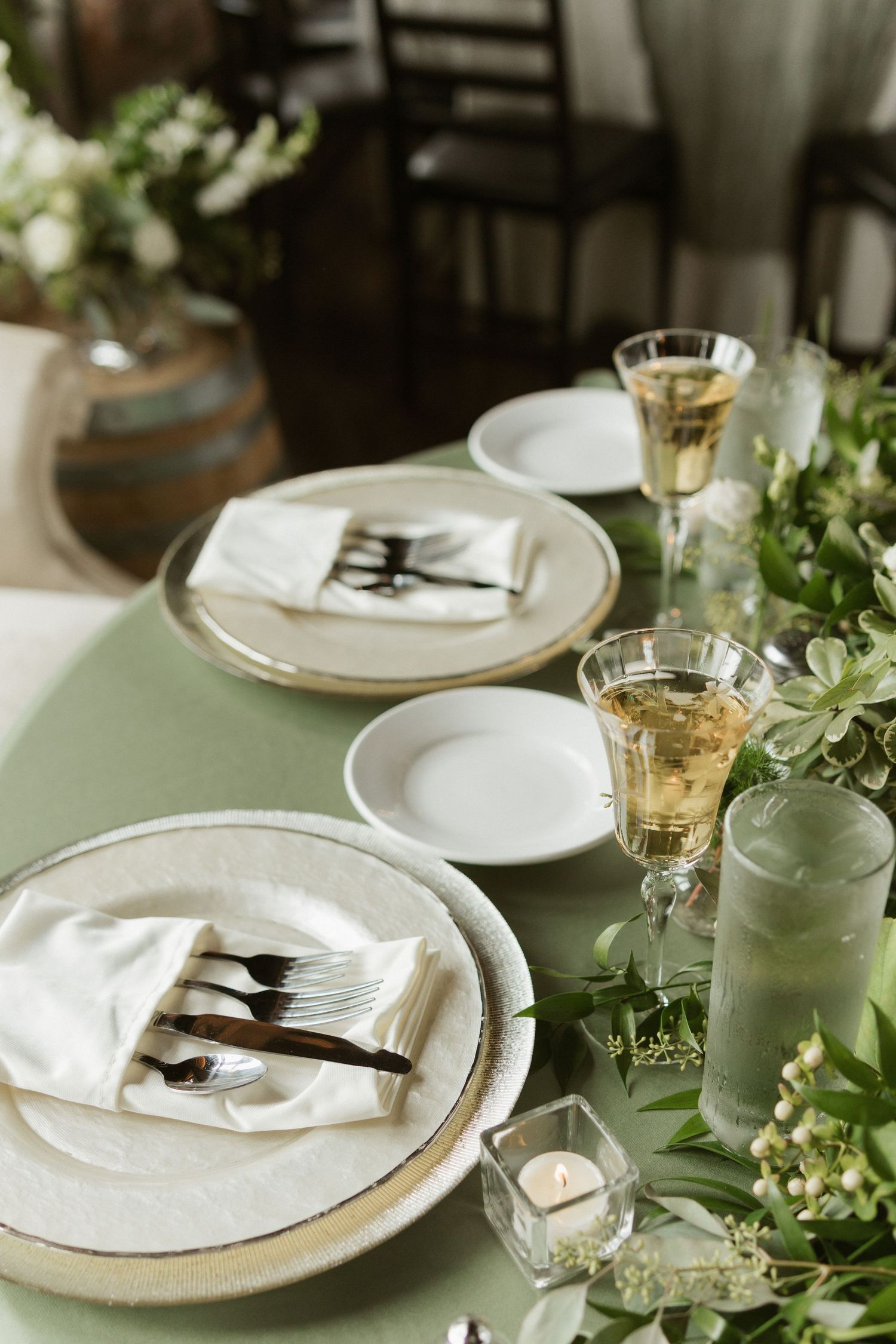 An elegant wedding table setting with white plates, gold chargers, and delicate greenery centerpieces.