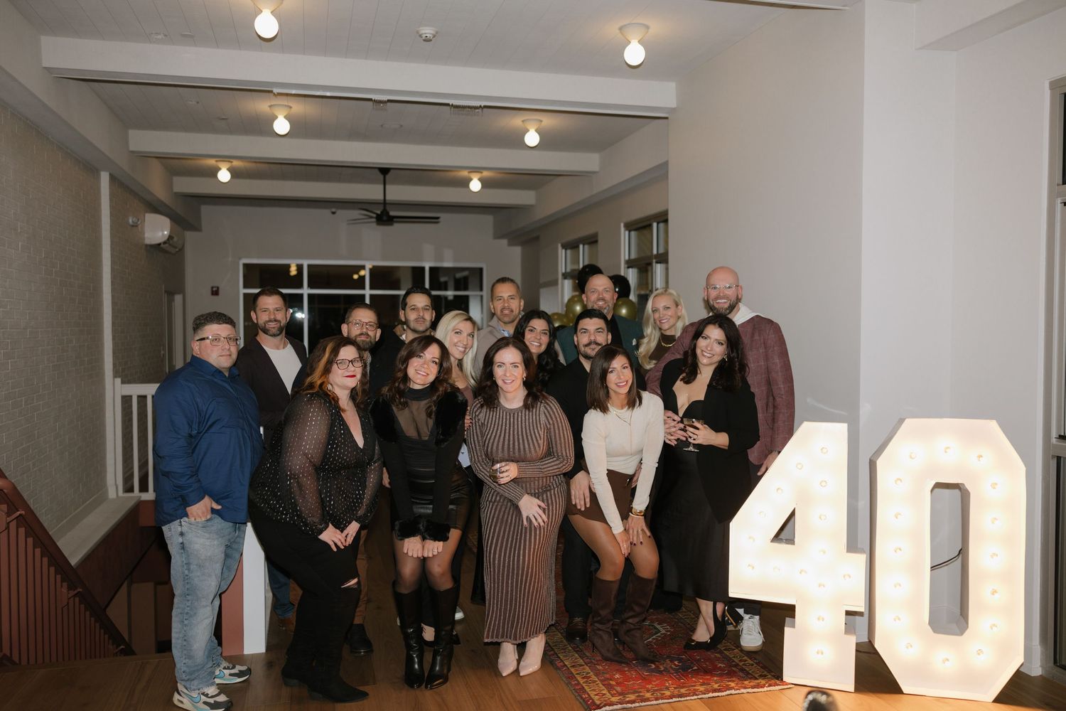 Group of adults posing together at a 40th birthday party celebration indoors with marquee number decorations.