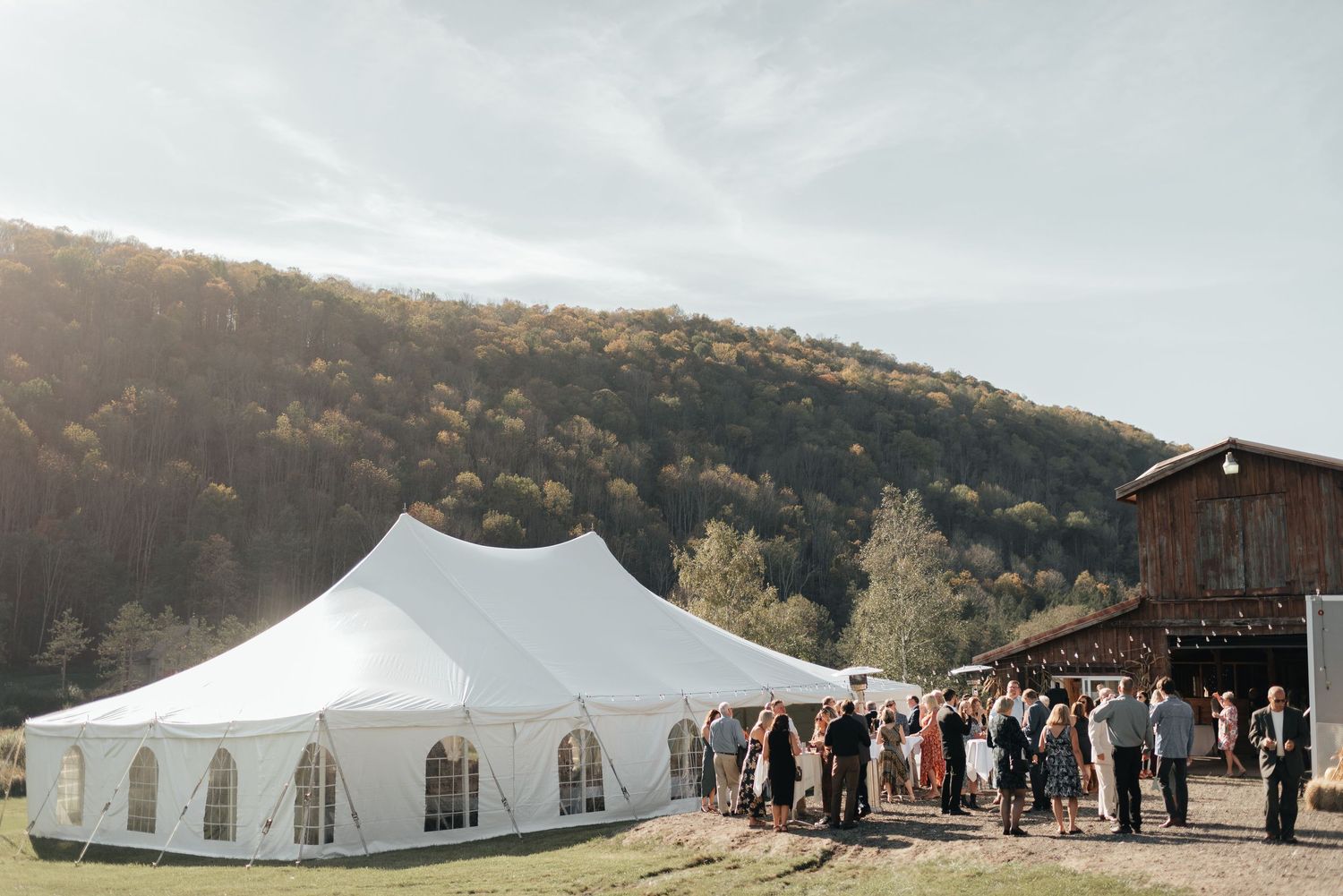 A white wedding tent stands elegantly against a scenic mountain backdrop during an outdoor celebration.