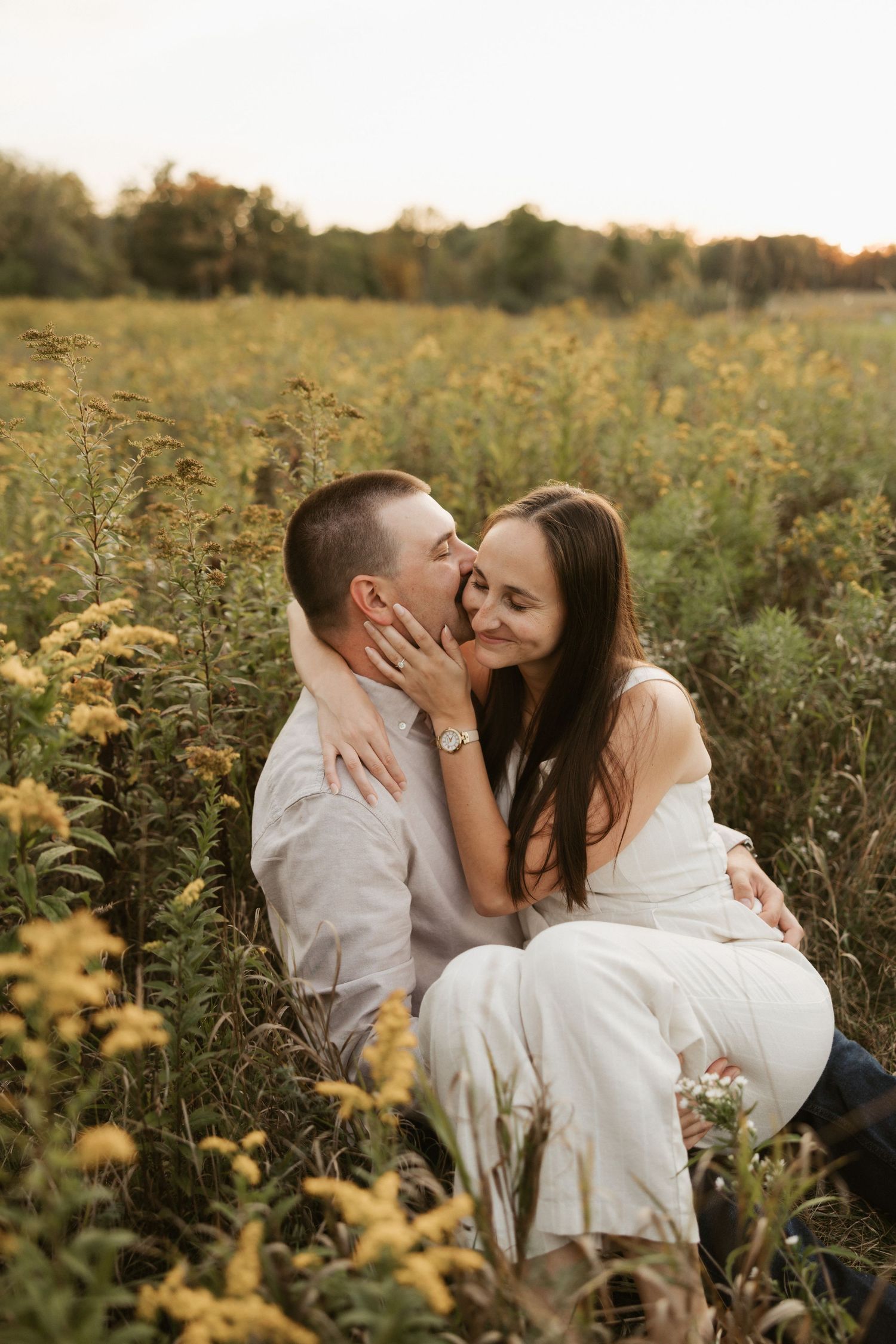 A romantic couple embraces in a golden wildflower field during sunset.