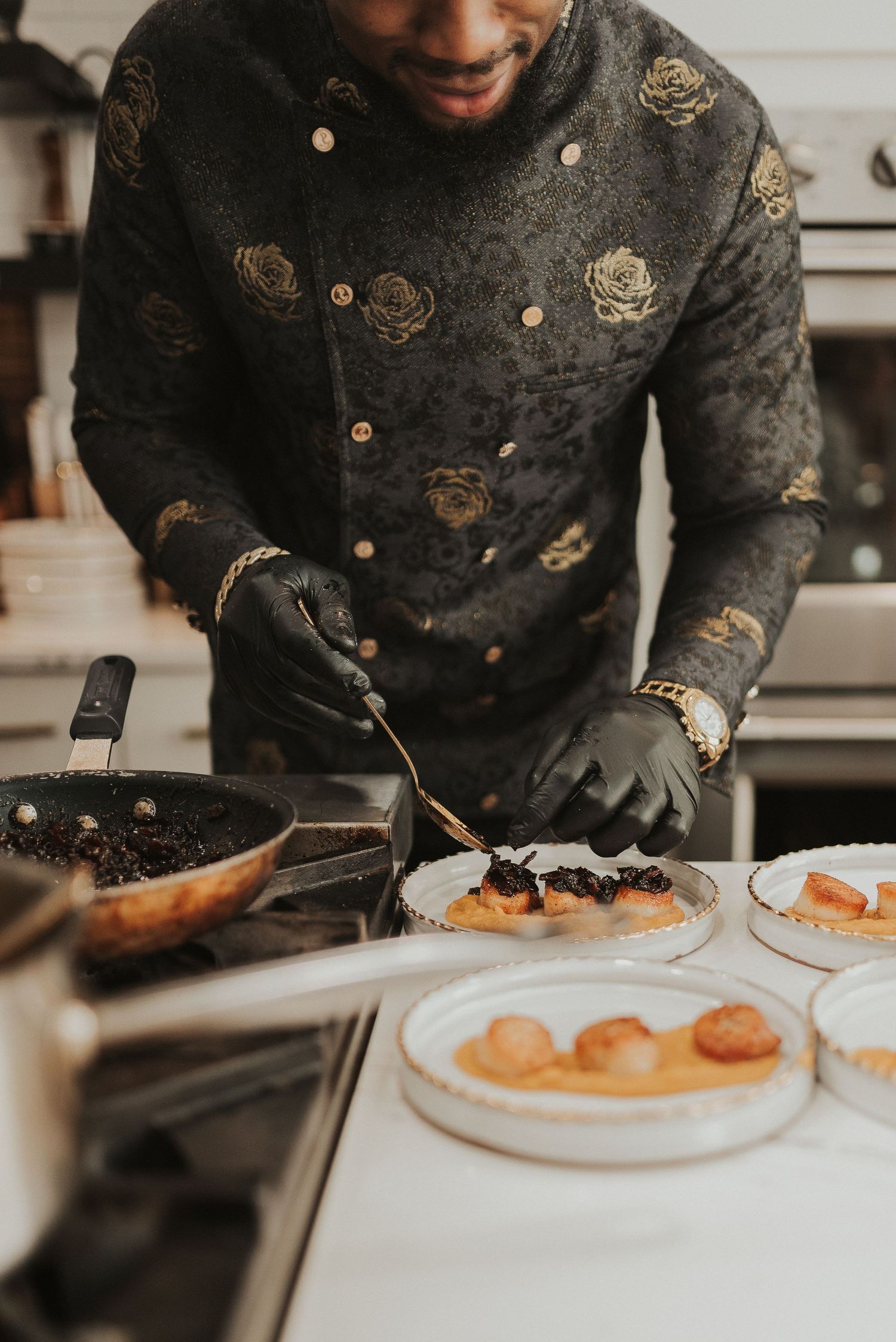 A chef in a black embroidered uniform plates gourmet food on white dishes at a restaurant.