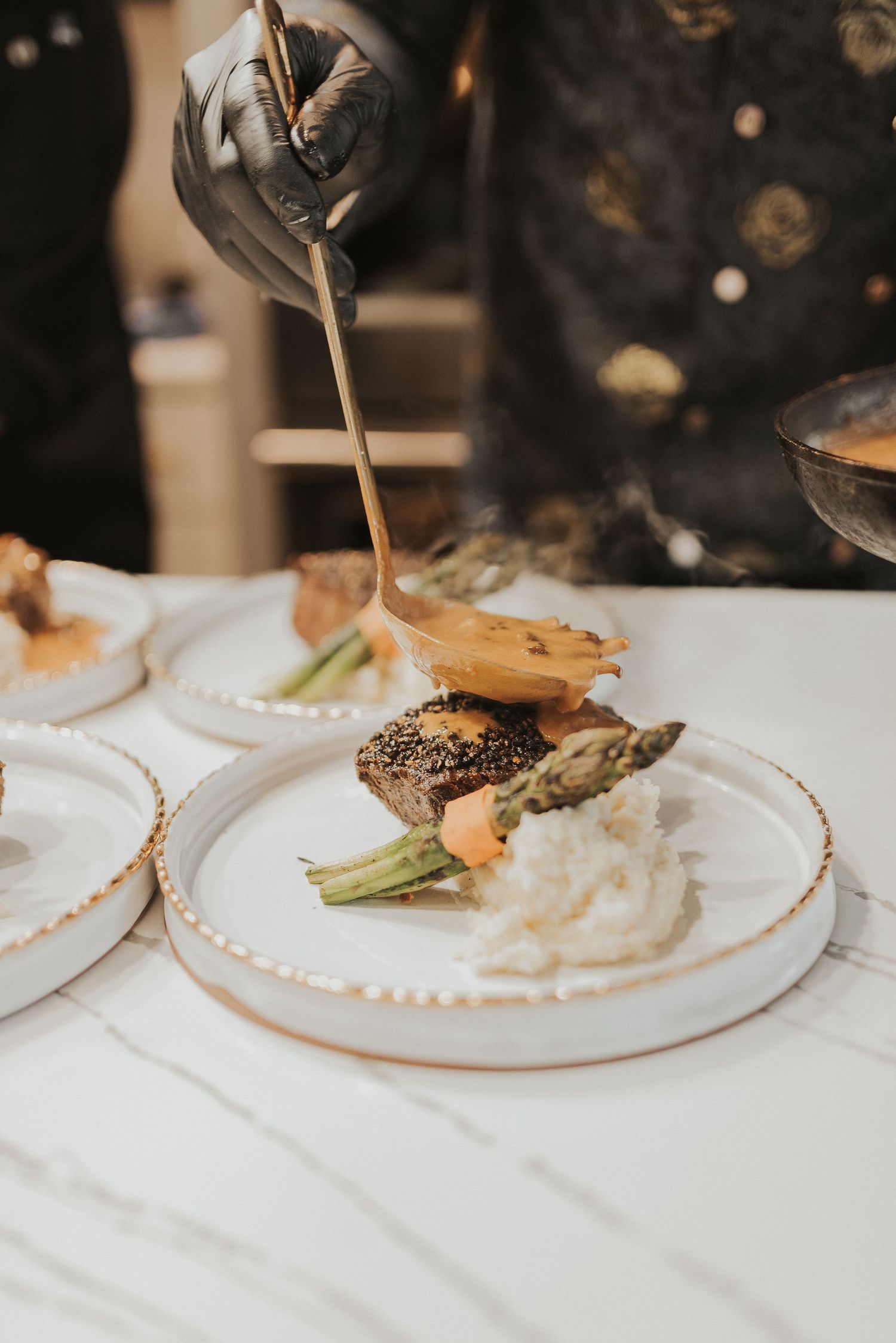 Elegant plated dishes with sauces being poured over white plates in a fine dining restaurant setting.