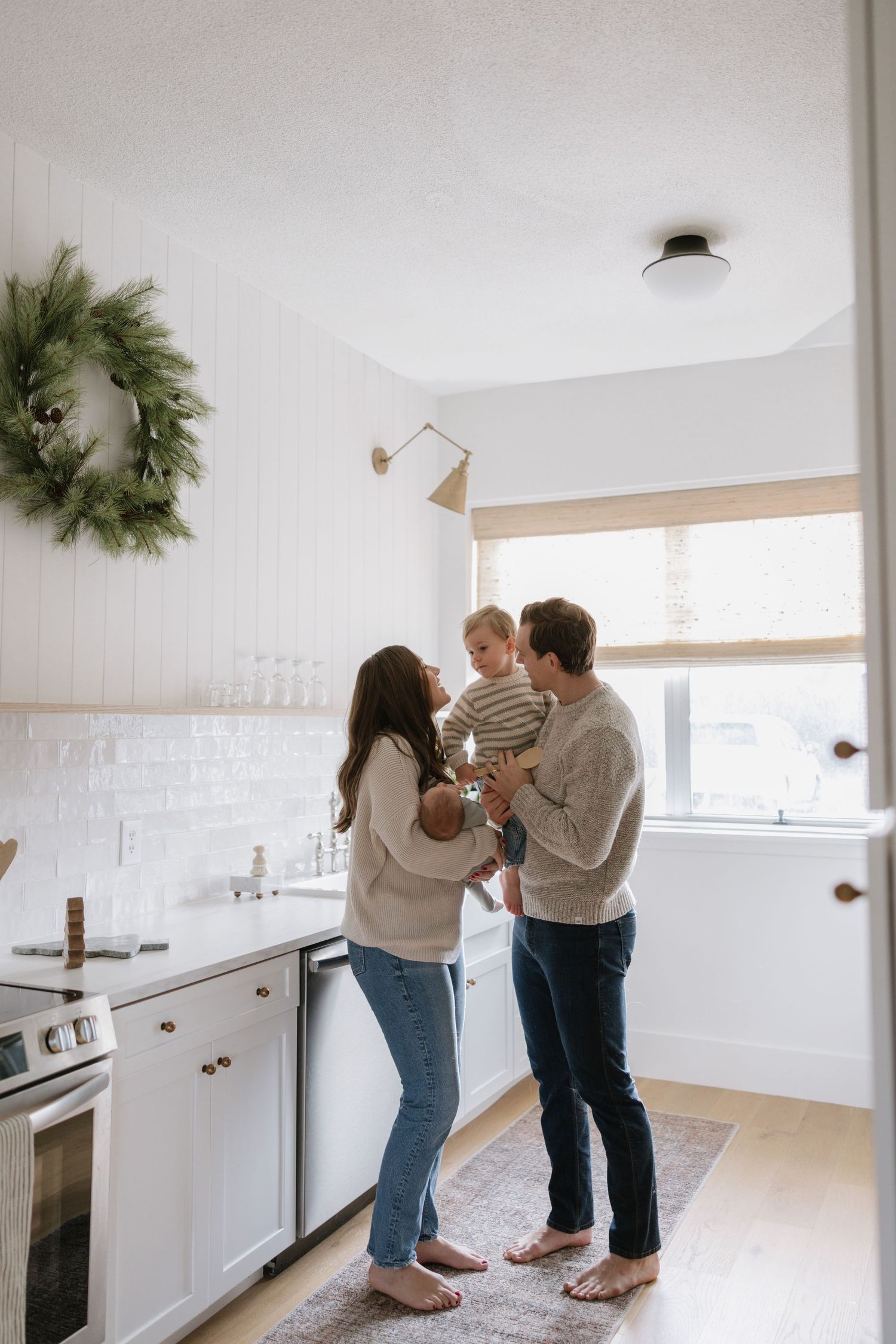 A family stands together in a bright modern white kitchen with hardwood floors and minimalist decor.