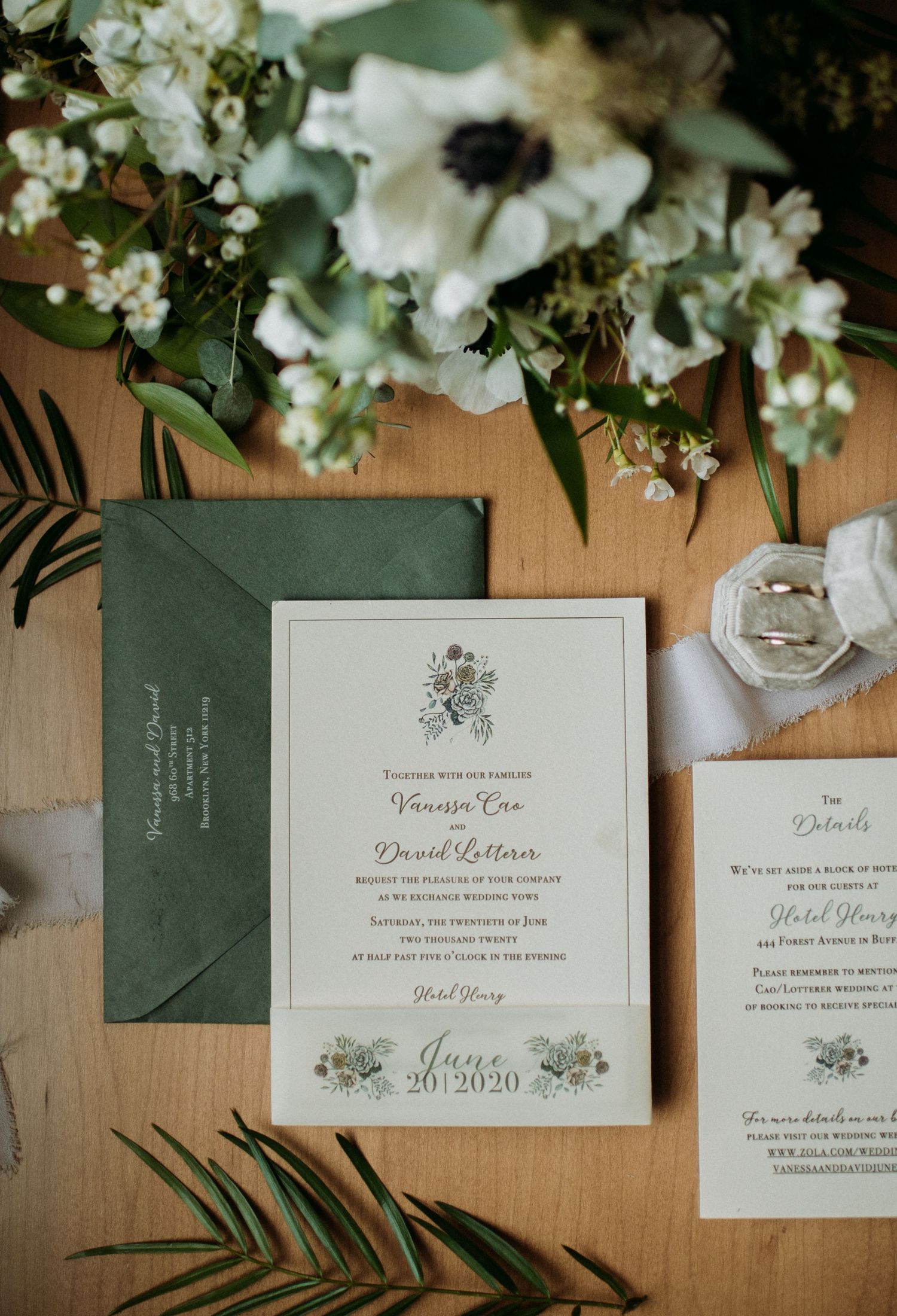Elegant wedding invitation suite in sage green and cream with floral details and calligraphy displayed with white flowers.