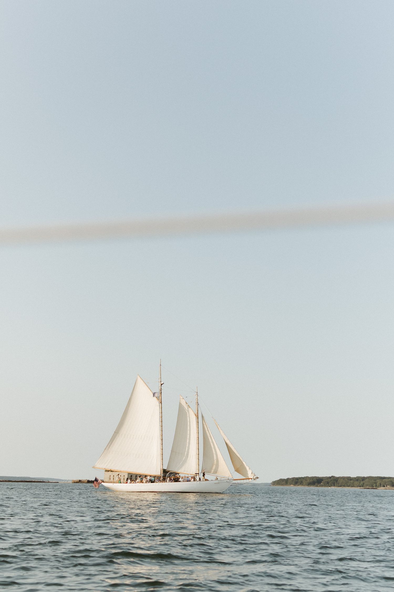 A white-sailed schooner glides gracefully across calm waters on the horizon during a peaceful day at sea.