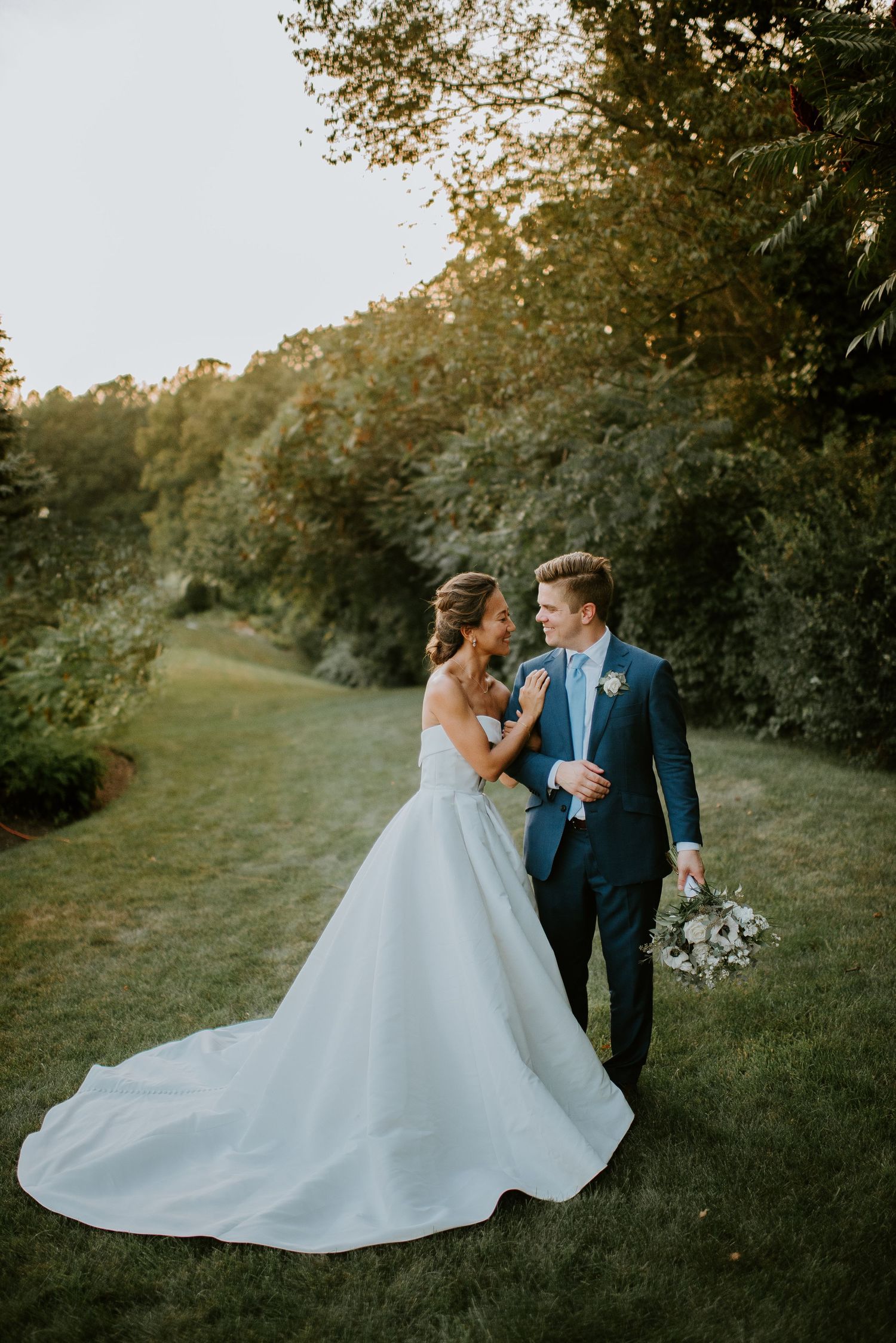 A romantic wedding couple shares a tender moment at sunset in a lush green outdoor setting.