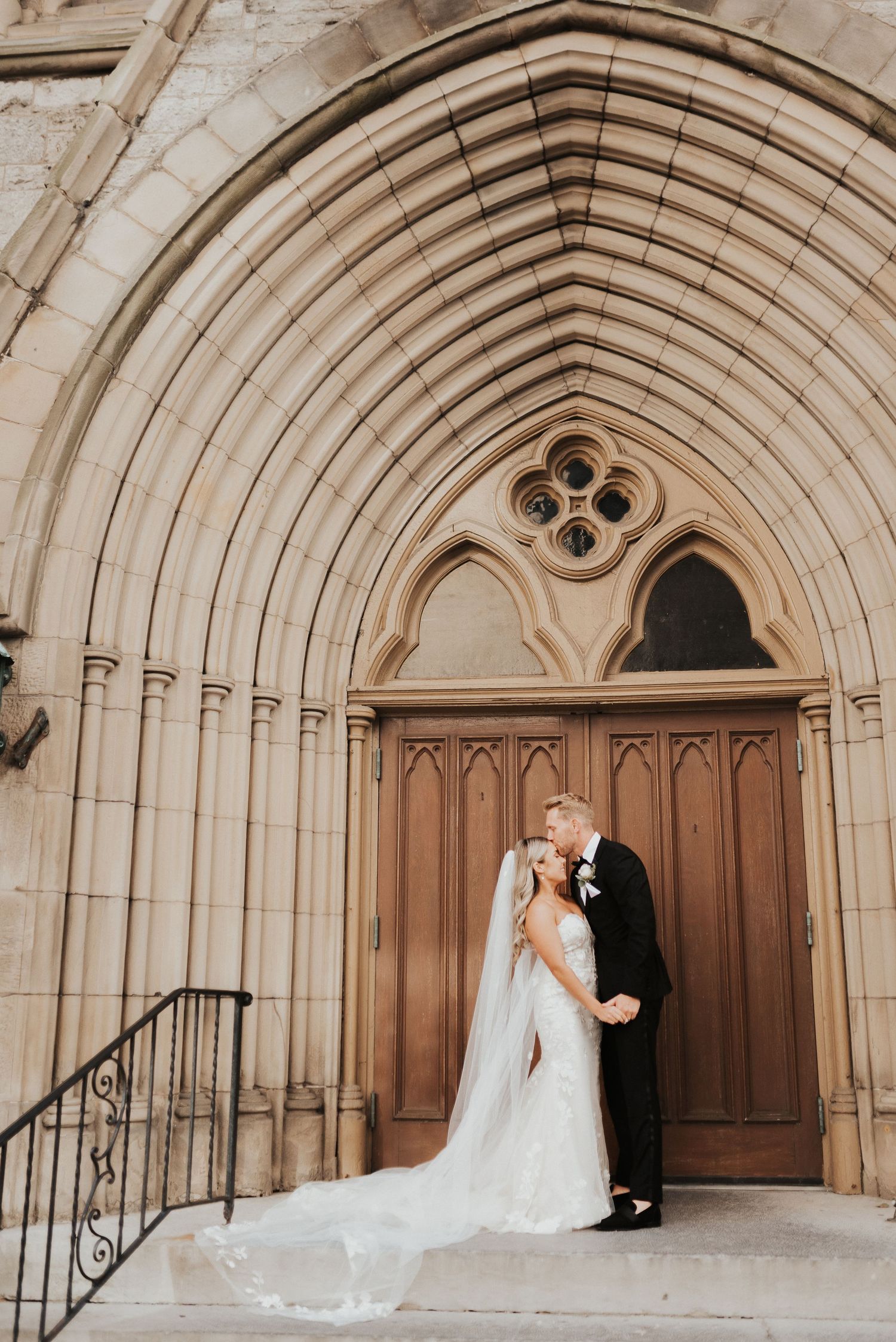 Wedding couple poses in sequence under grand stone archway of historic church entrance.