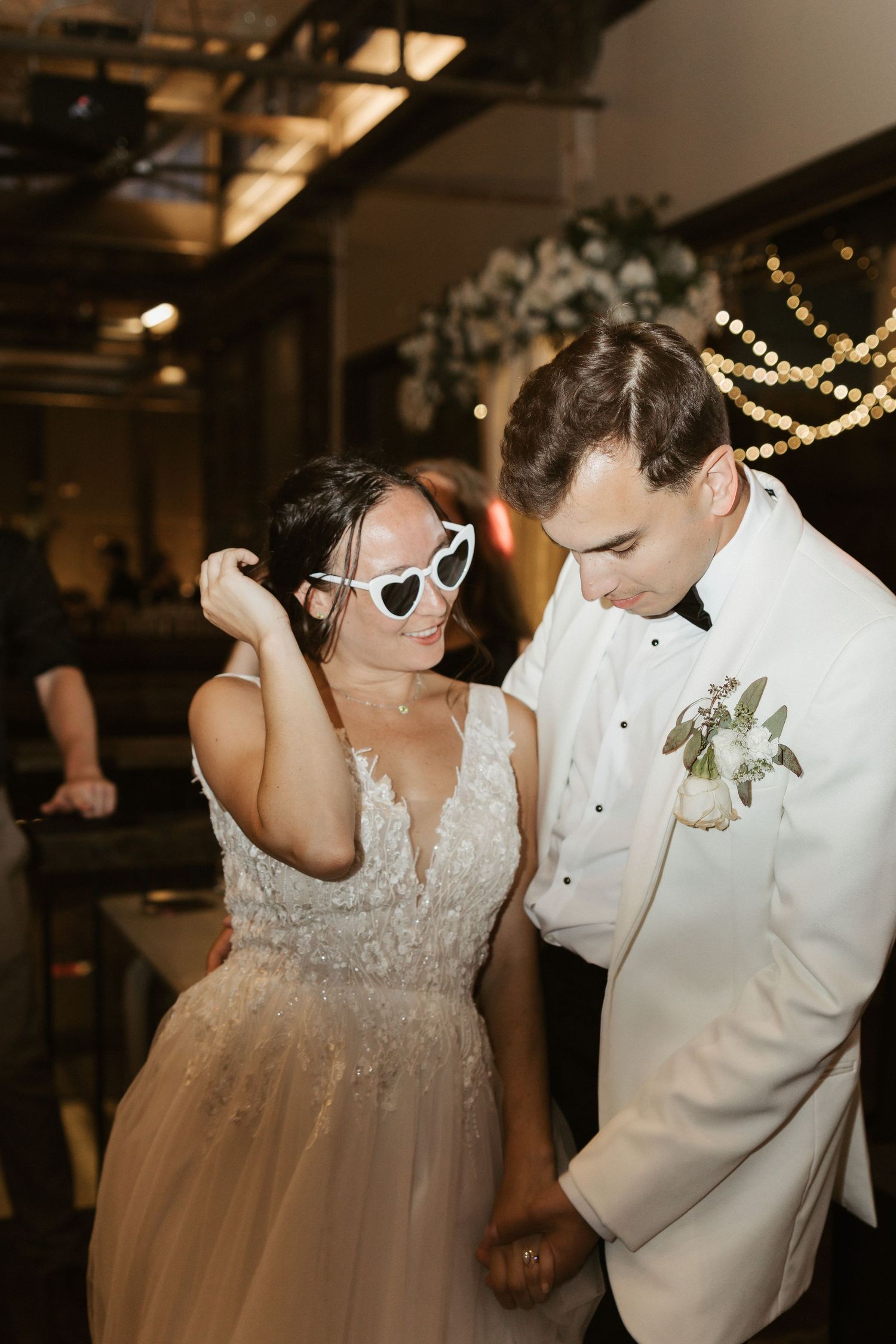 Bride and groom dancing together at their wedding reception under warm lighting and string lights.