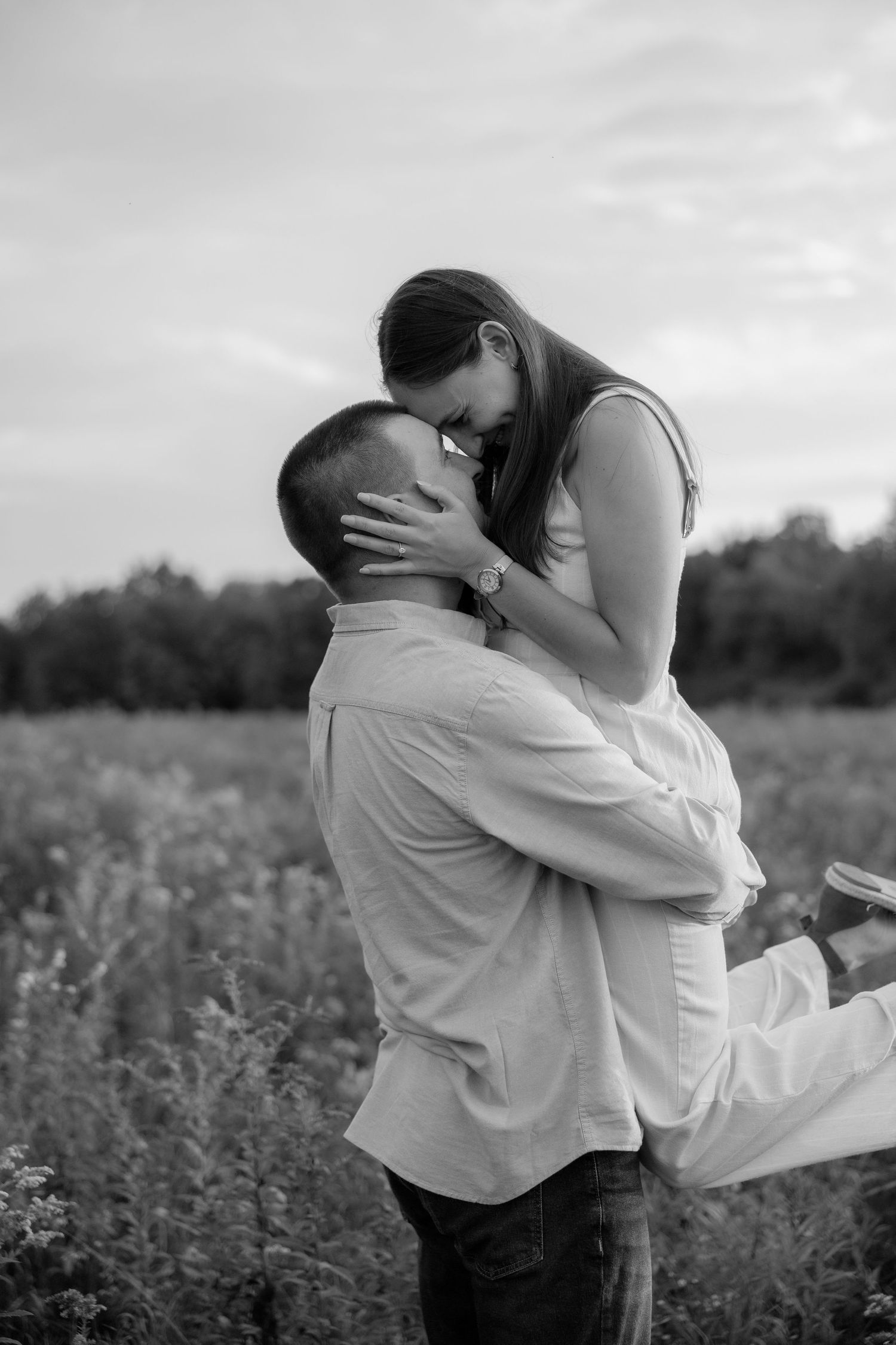 A romantic couple embraces in a field during an outdoor photoshoot in black and white.