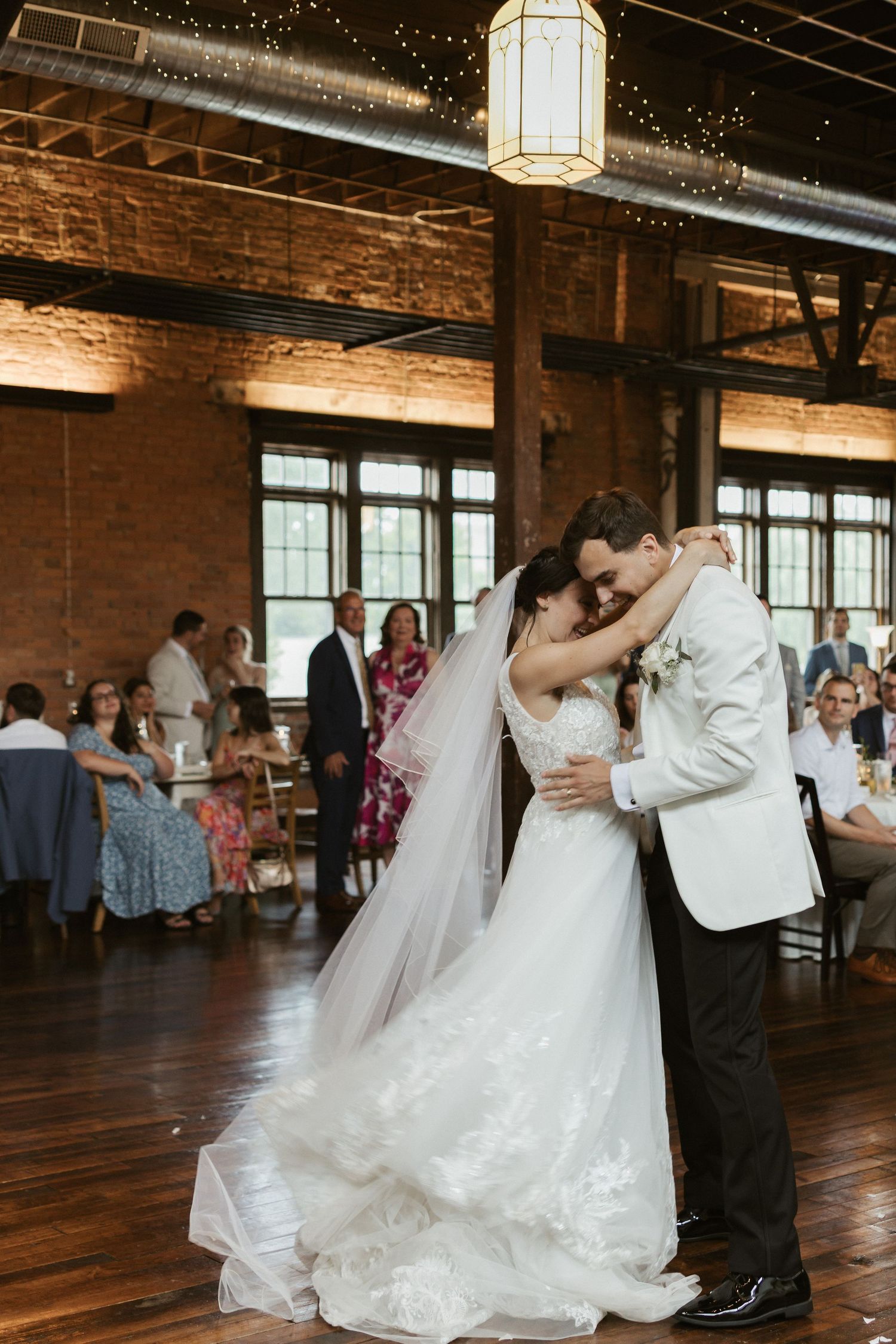 Wedding couple shares a romantic dip during their first dance on a rustic wooden dance floor with exposed brick walls.