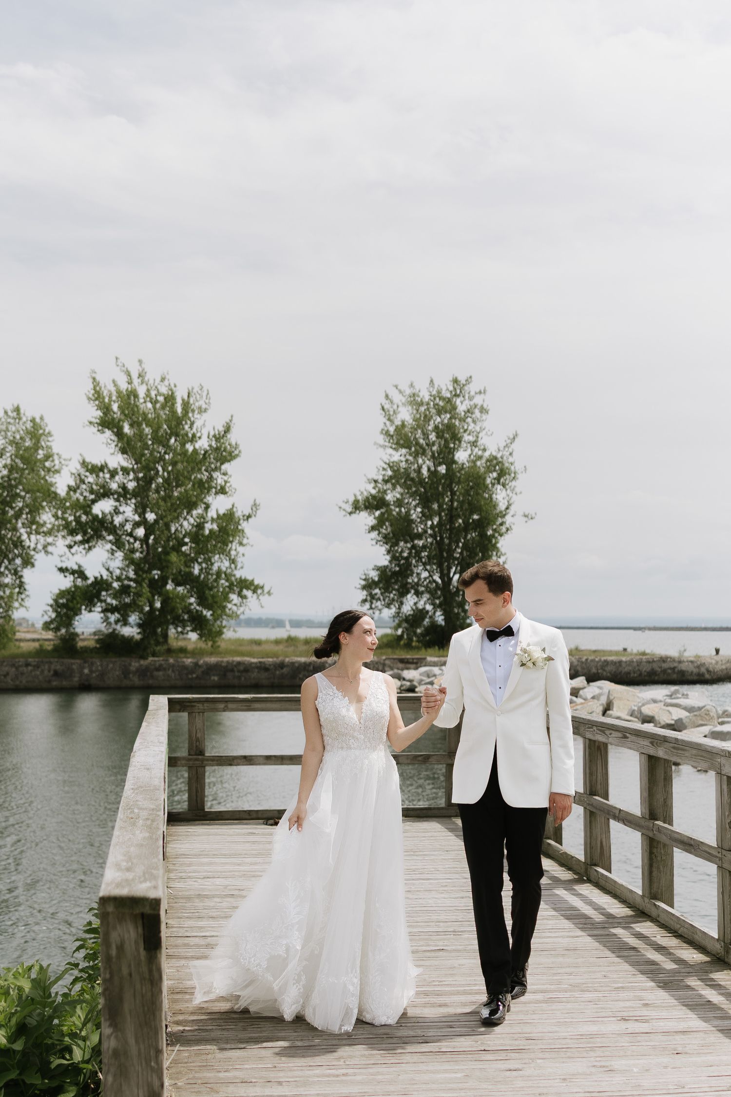 A couple in wedding attire walks along a wooden boardwalk by the water on their special day.