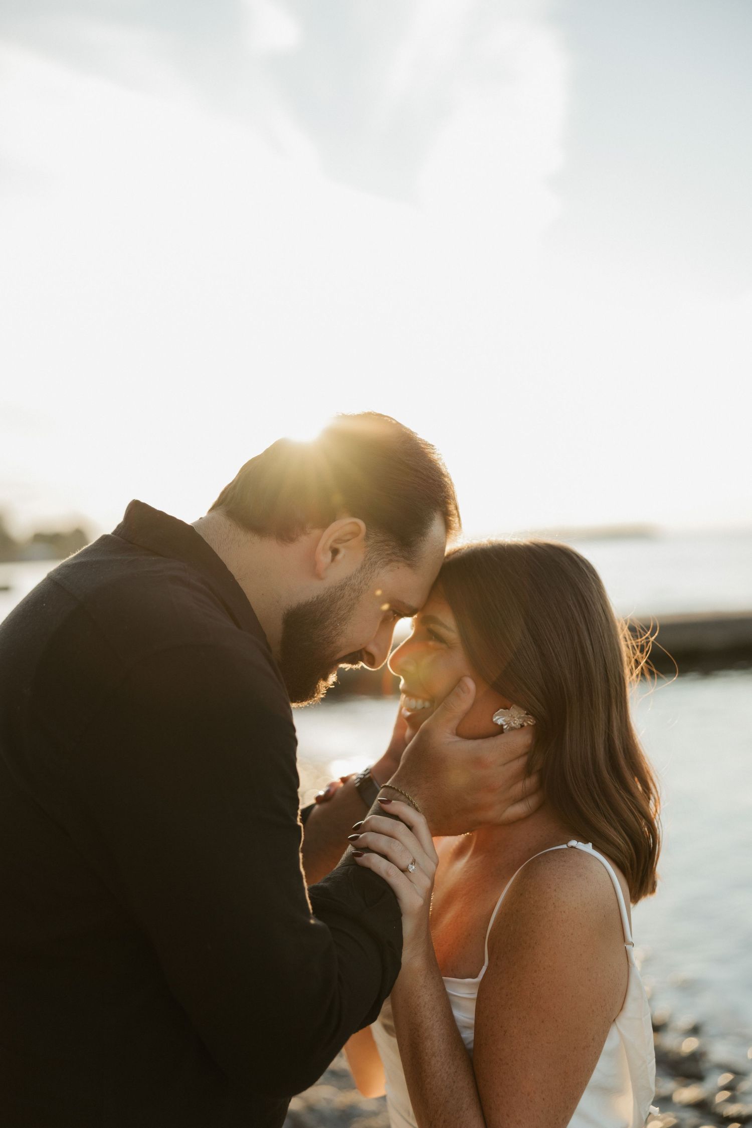 Romantic couple sharing an intimate moment at sunset by the water with golden sunlight streaming between them.