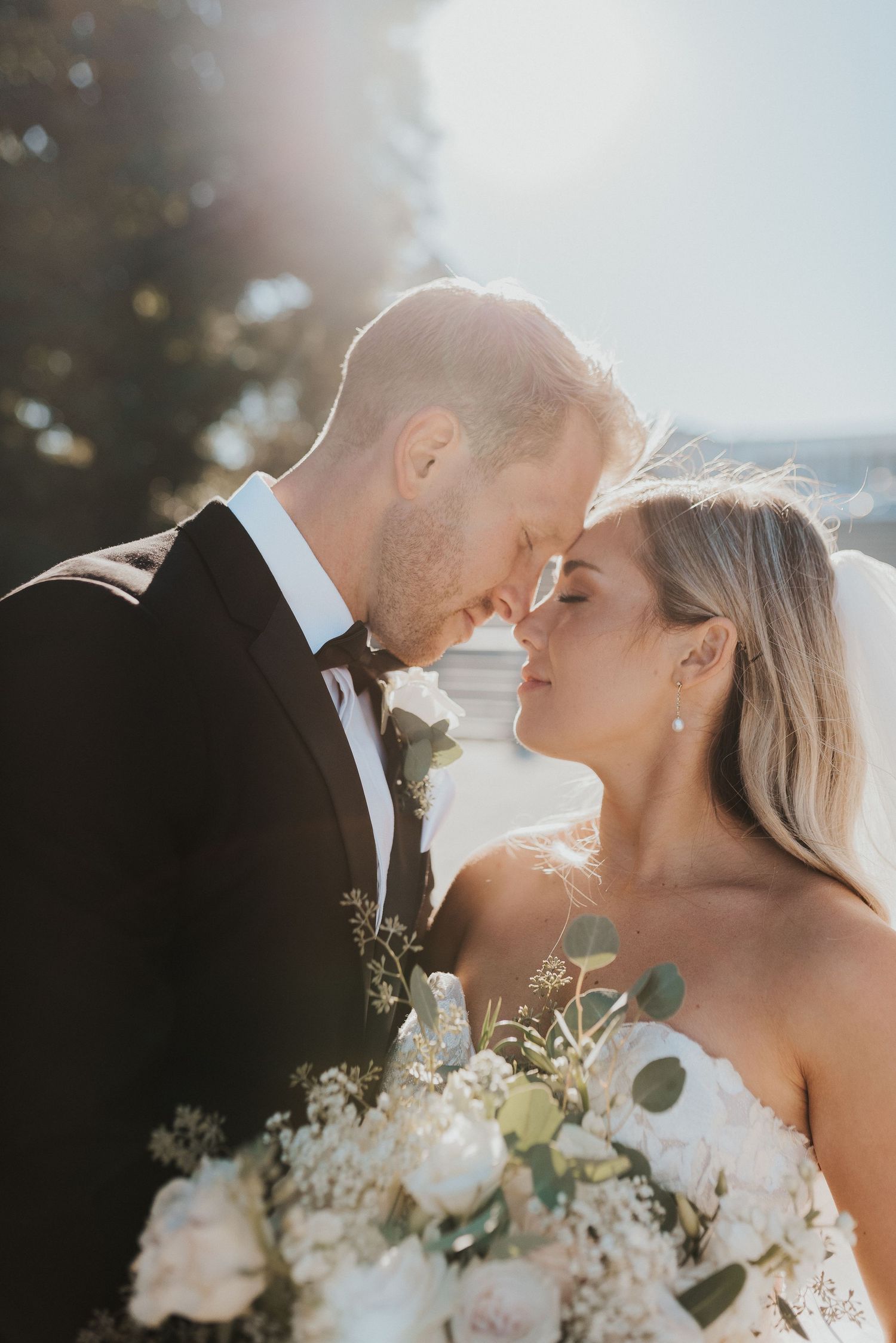 A sunlit wedding portrait with delicate white flowers and greenery bouquet creating a dreamy atmosphere.