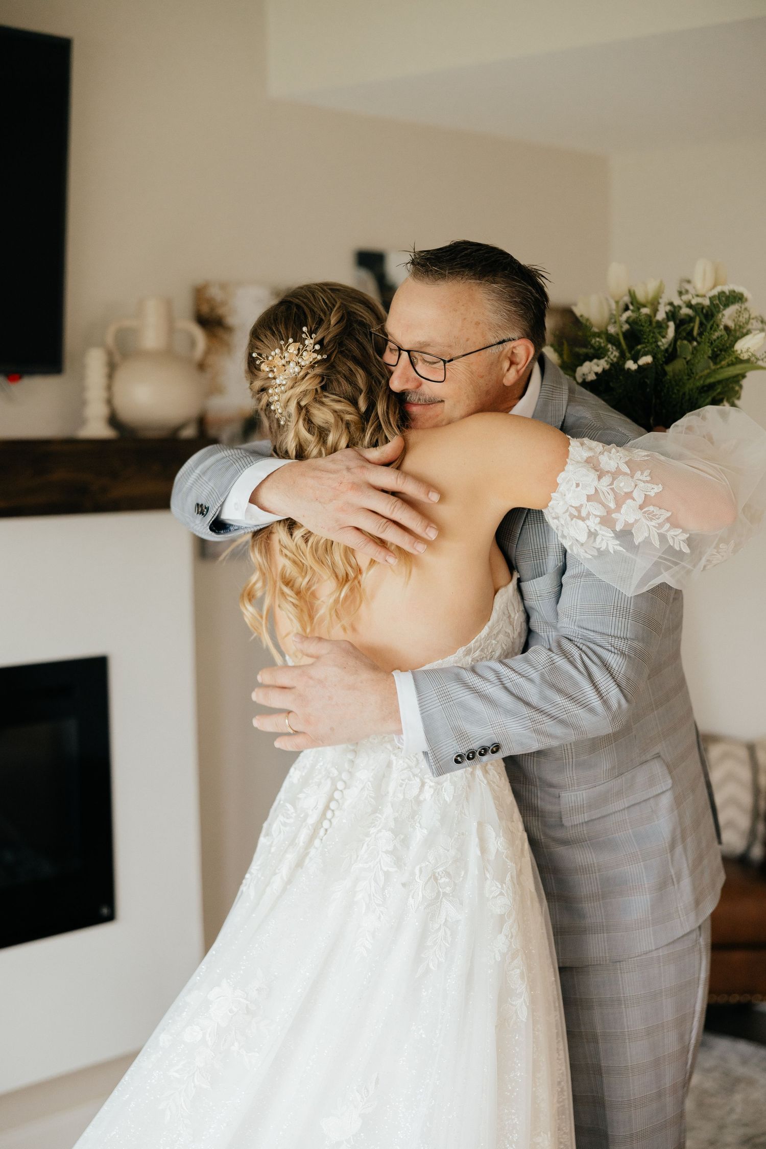 A tender first look moment between newlyweds as the bride in a white lace gown embraces the groom in a gray suit.