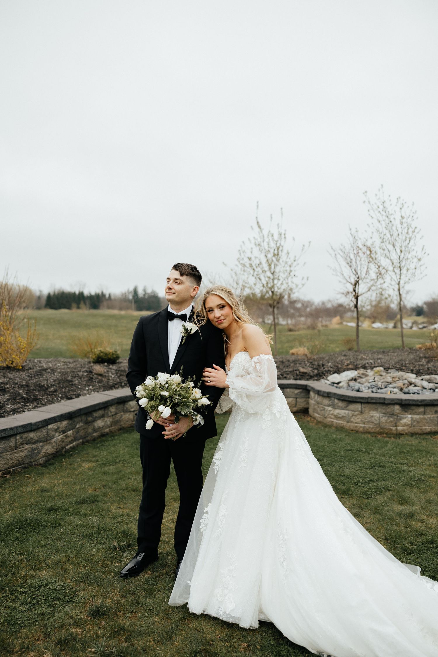 A romantic outdoor wedding photo session featuring a couple in formal attire on a cloudy day in a natural landscape.