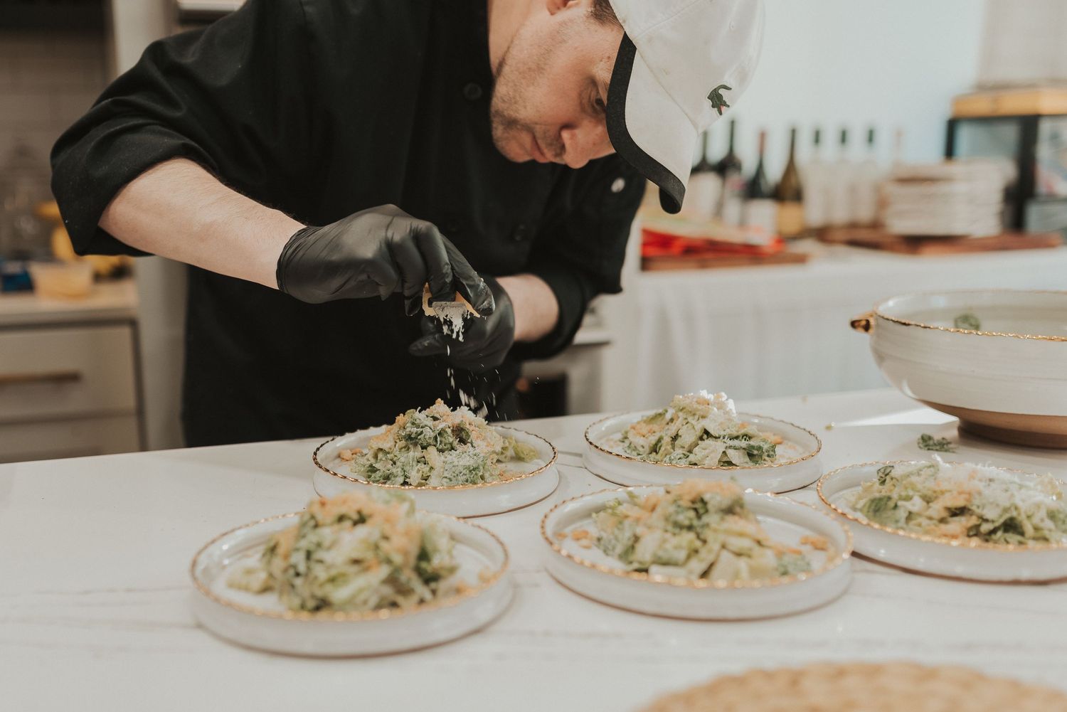 Chef plates creamy pasta dishes with garnish on white plates in a professional kitchen setting.
