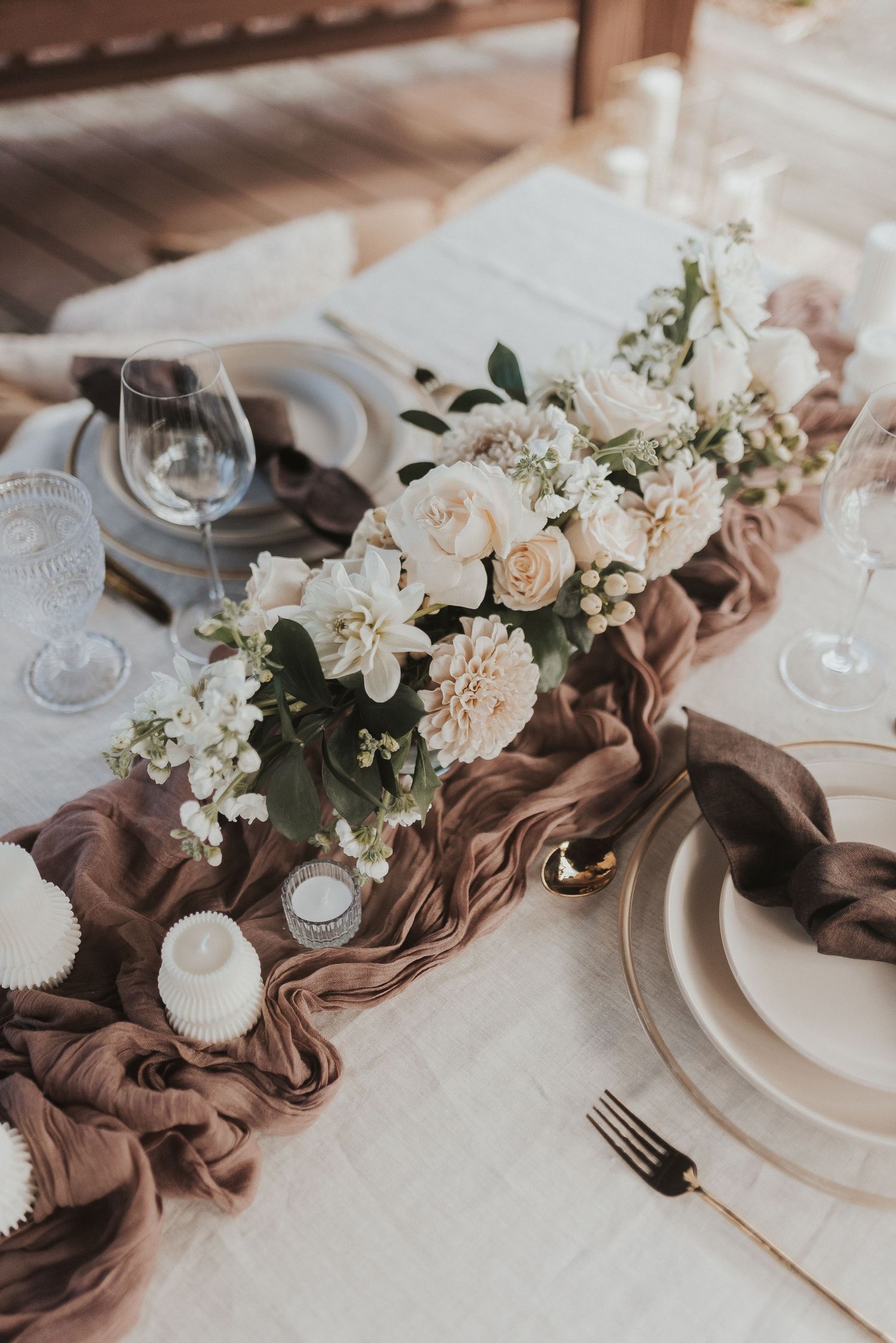 Elegant wedding table setting with brown linen runner, white roses, and delicate place settings in a rustic style.