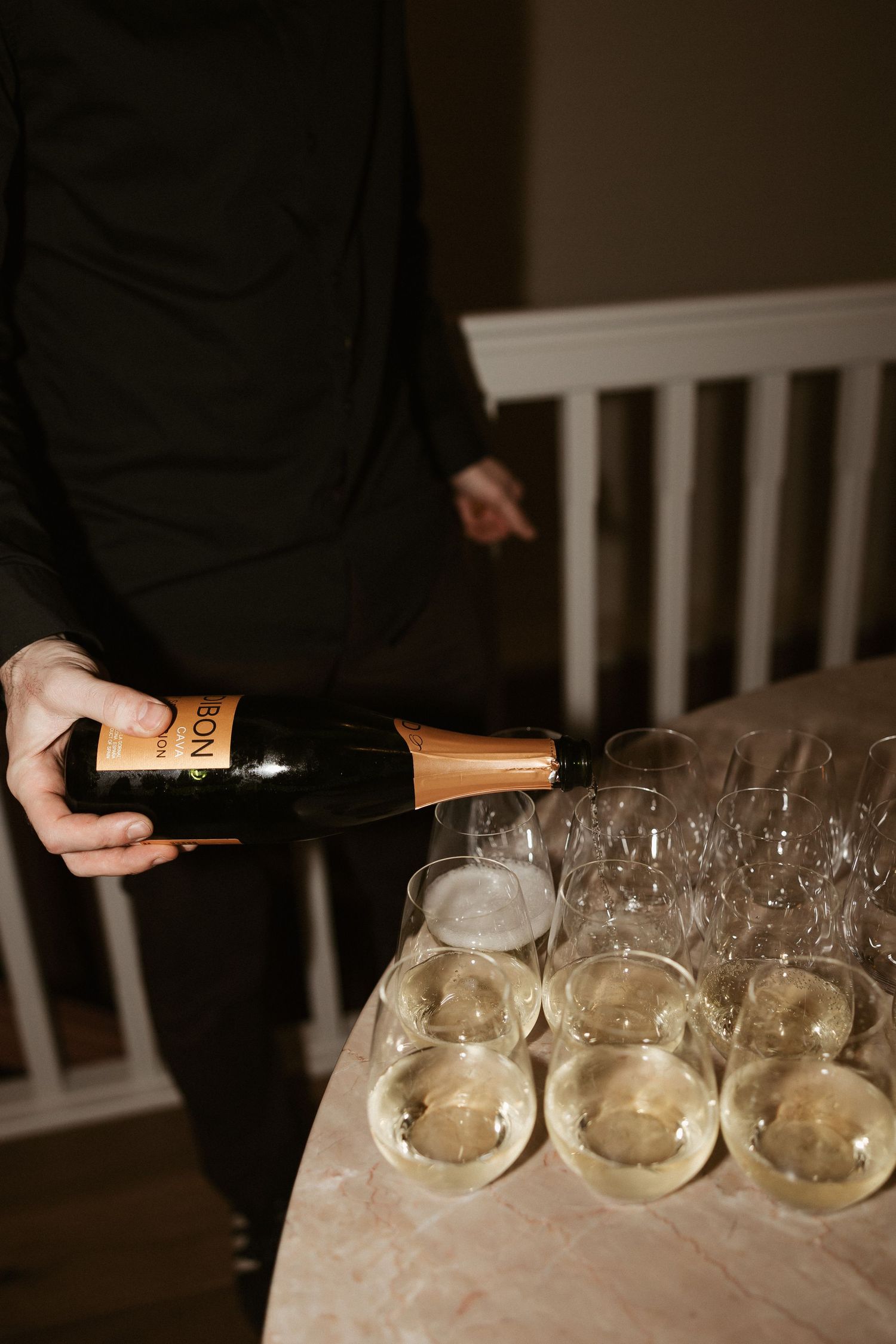 Person pouring champagne into elegant glasses at a celebration event, with a bottle of sparkling wine on a round table.