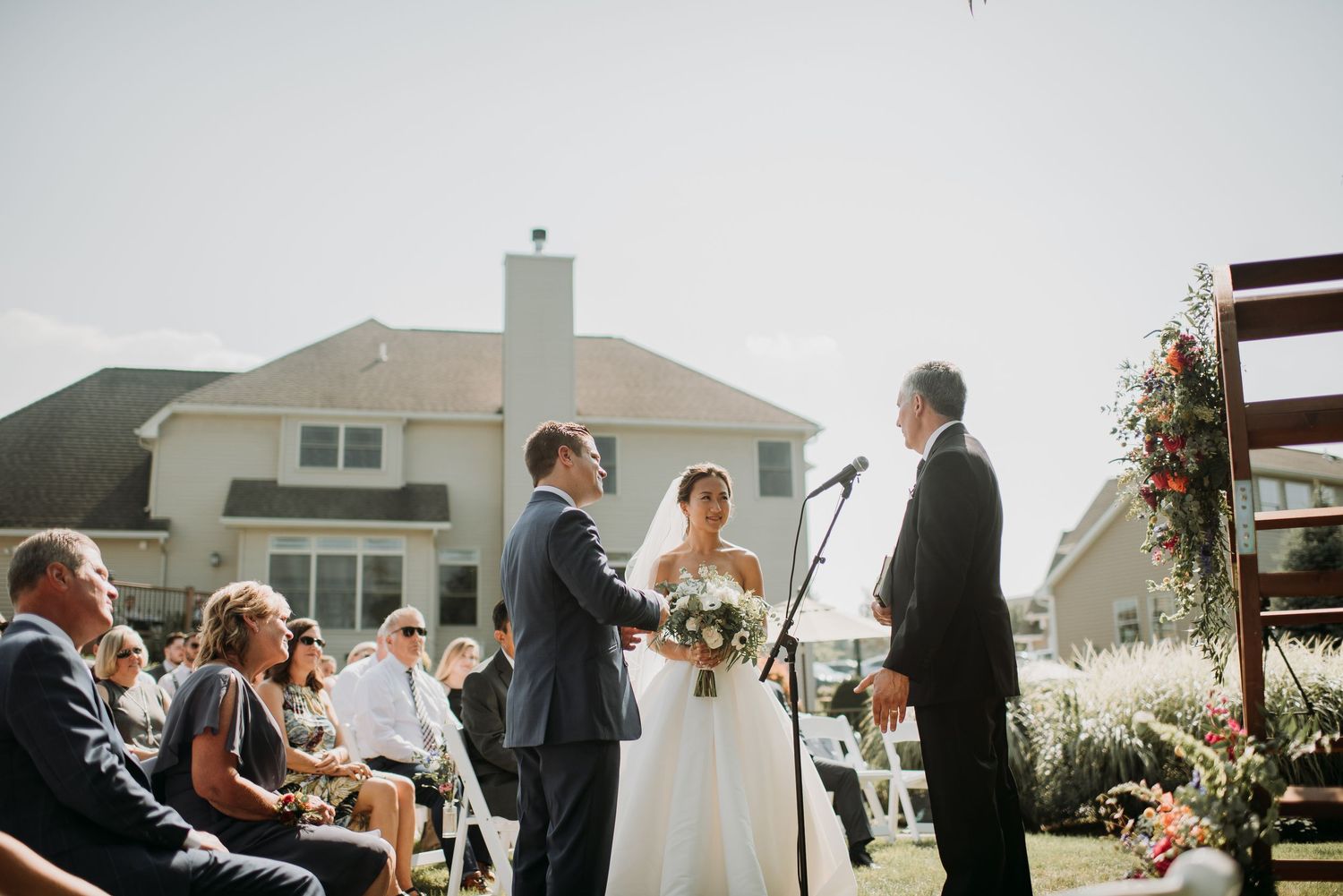 Wedding guests gather under a white tent on a cloudy day during an outdoor ceremony celebration.