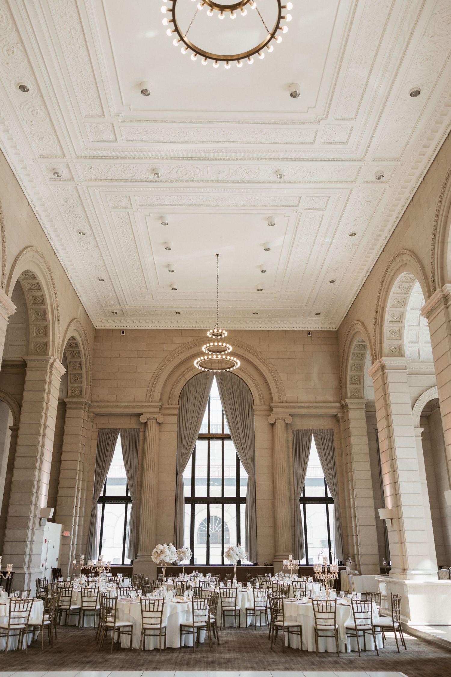 Elegant ballroom with high ceilings, crystal chandeliers, arched windows and white chiavari chairs set for a formal reception.