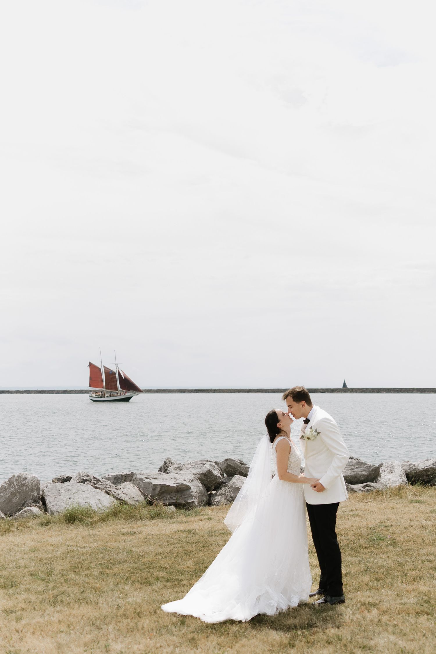 A seaside wedding photoshoot with a sailboat visible in the background on a cloudy day.