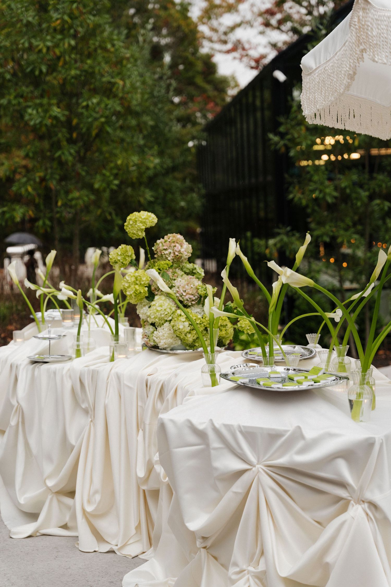 Elegant outdoor wedding reception tables set with white linens, crystal glassware and fresh green floral centerpieces.