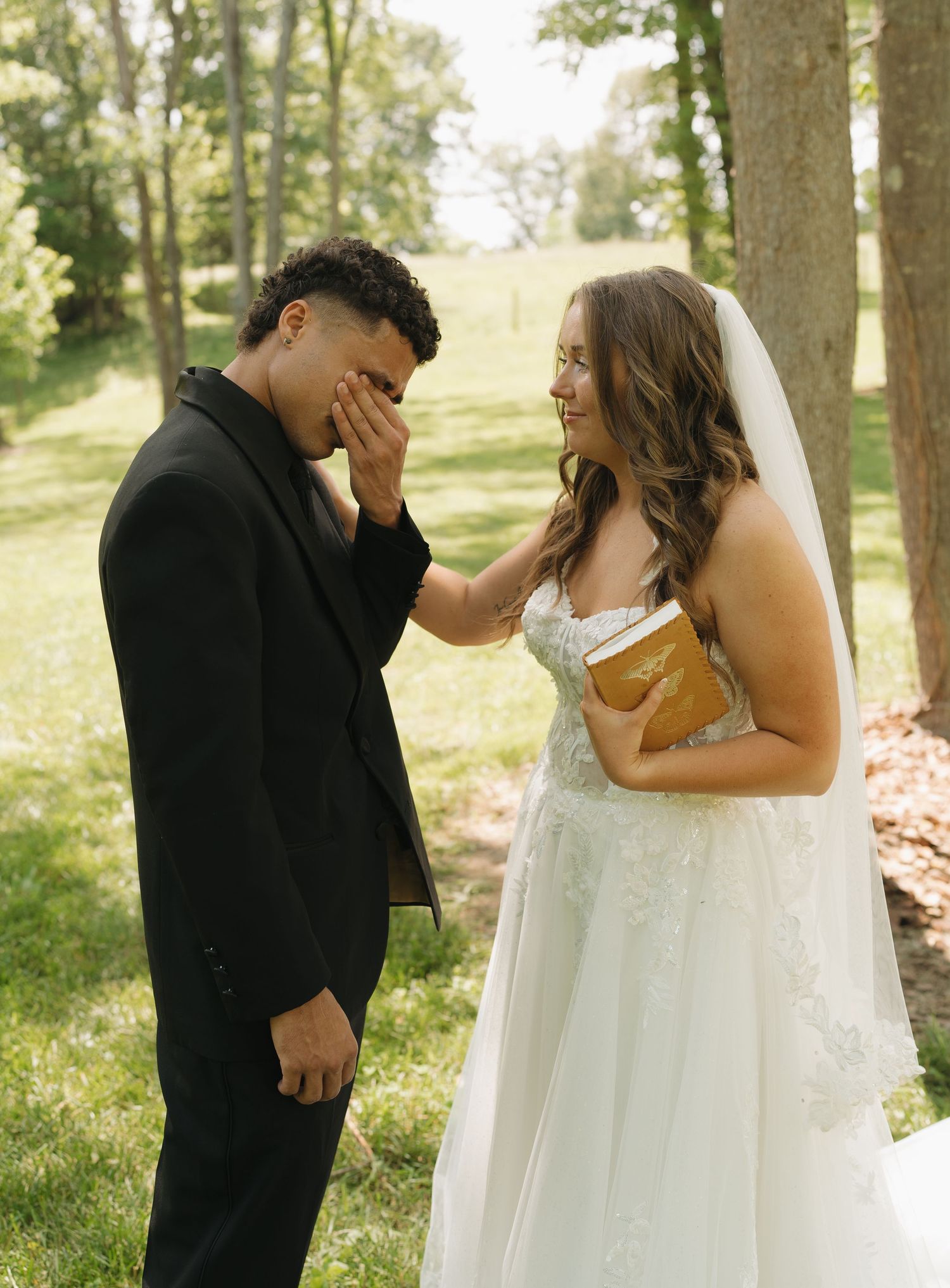 An emotional wedding moment captured outdoors with a couple sharing a tender reaction in natural lighting.