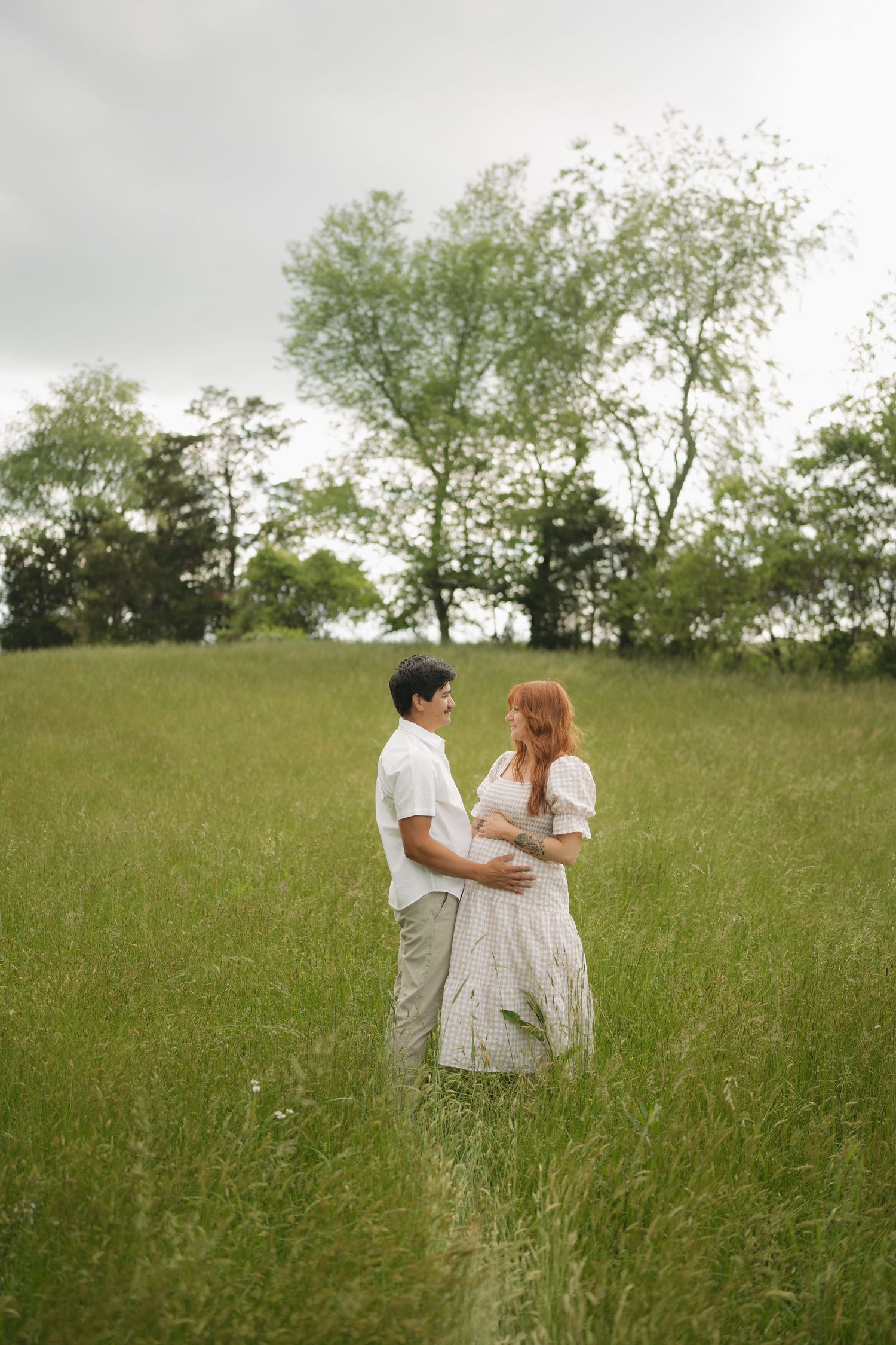 Couple in casual wedding attire stands together in tall grass field.