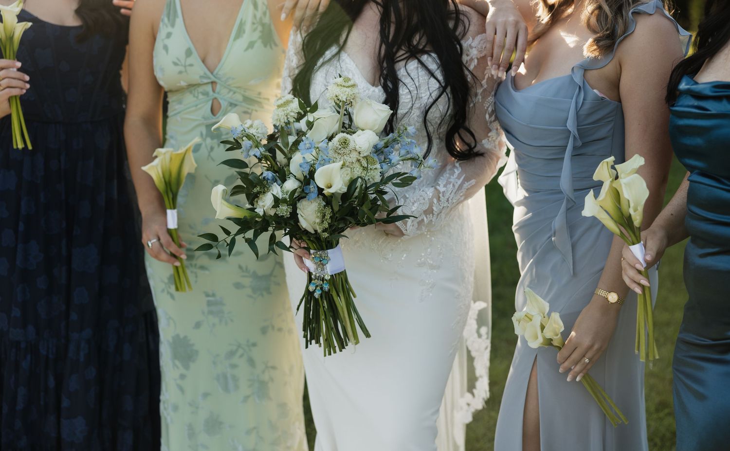 Wedding party holding elegant white and green floral bouquets in pastel dresses.