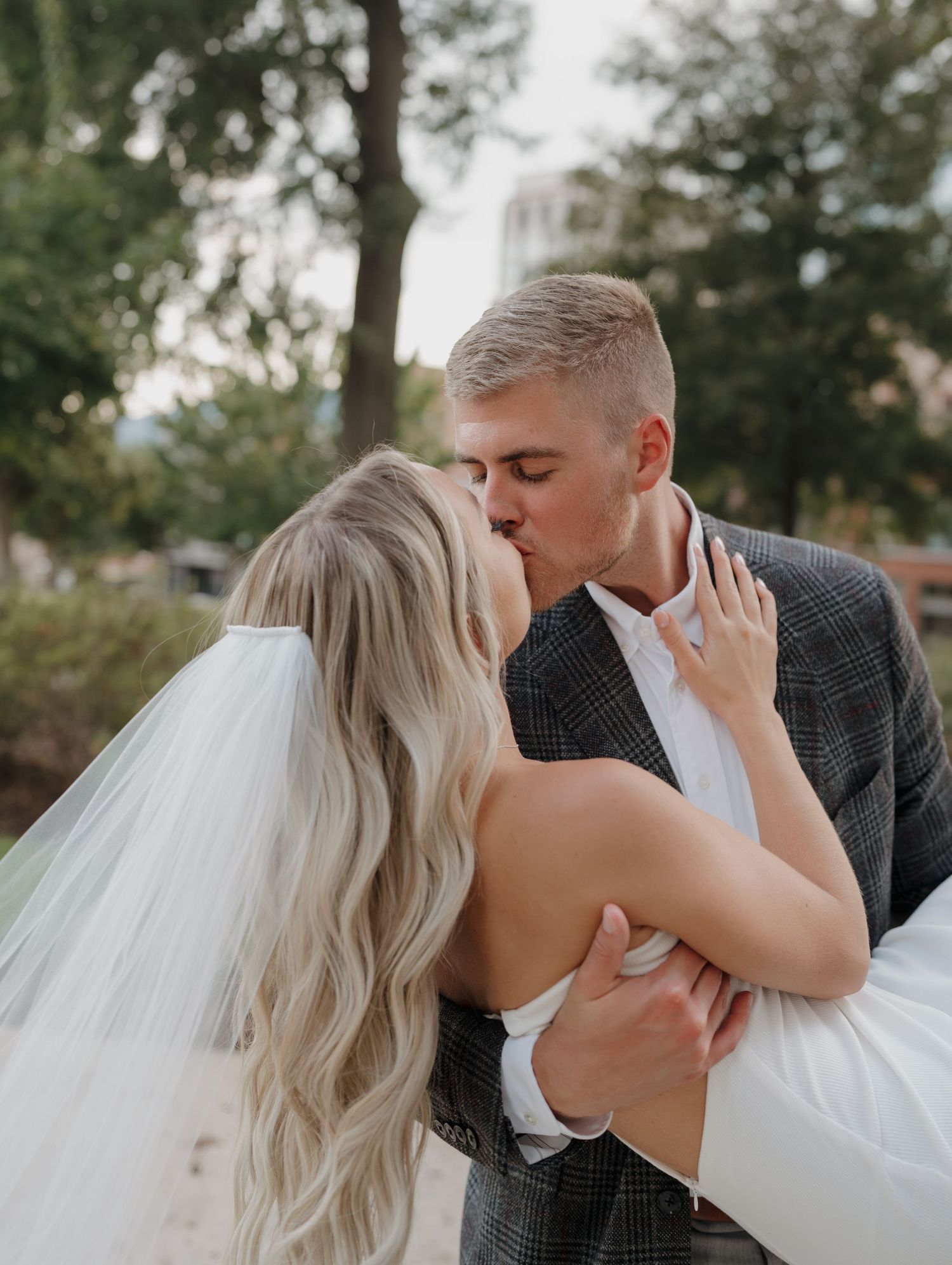 A romantic dip kiss between newlyweds, with bride in white dress and flowing veil.