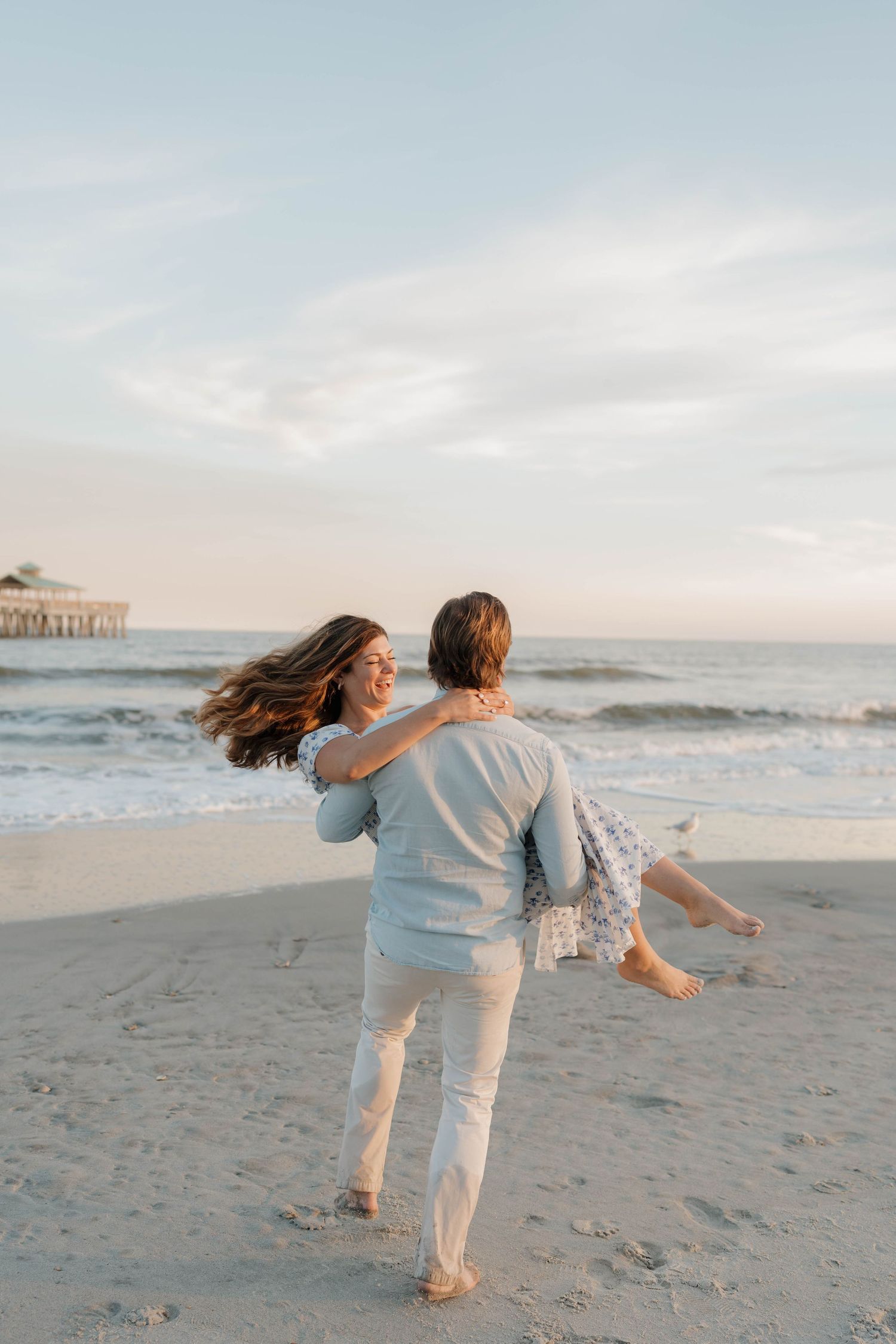 Couple playing on beach at sunset with pier in background.
