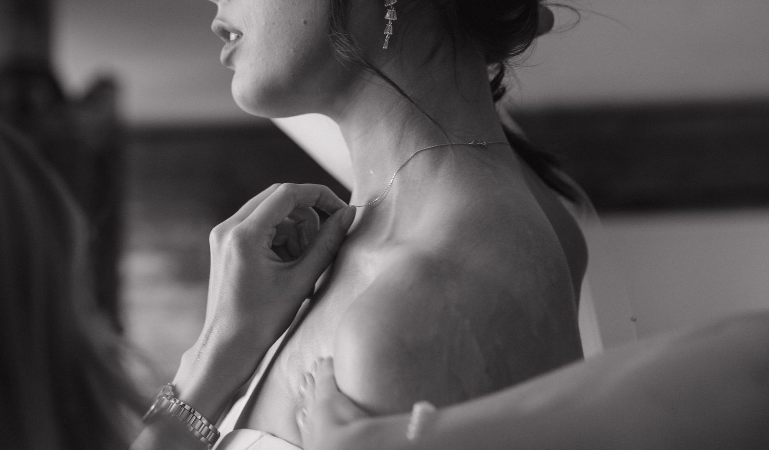 Black and white close-up of bridal preparations showing neckline and shoulder details.