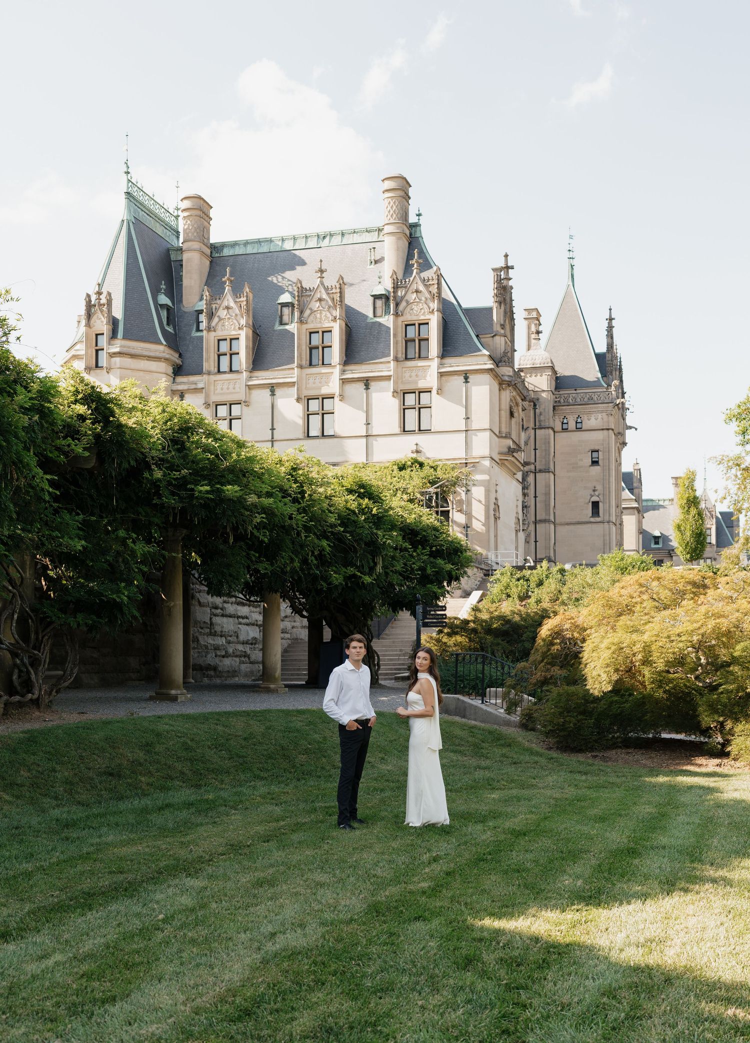 A couple poses together on a grassy lawn with a majestic stone castle in the background during their wedding photoshoot.