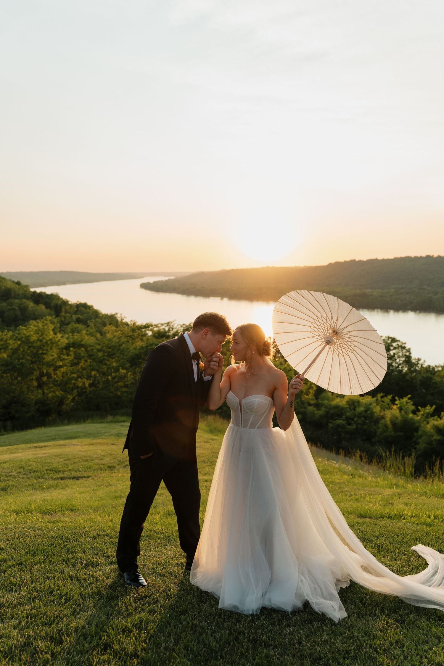 A romantic sunset wedding photo series with white parasols and rolling hills overlooking a lake in the background.