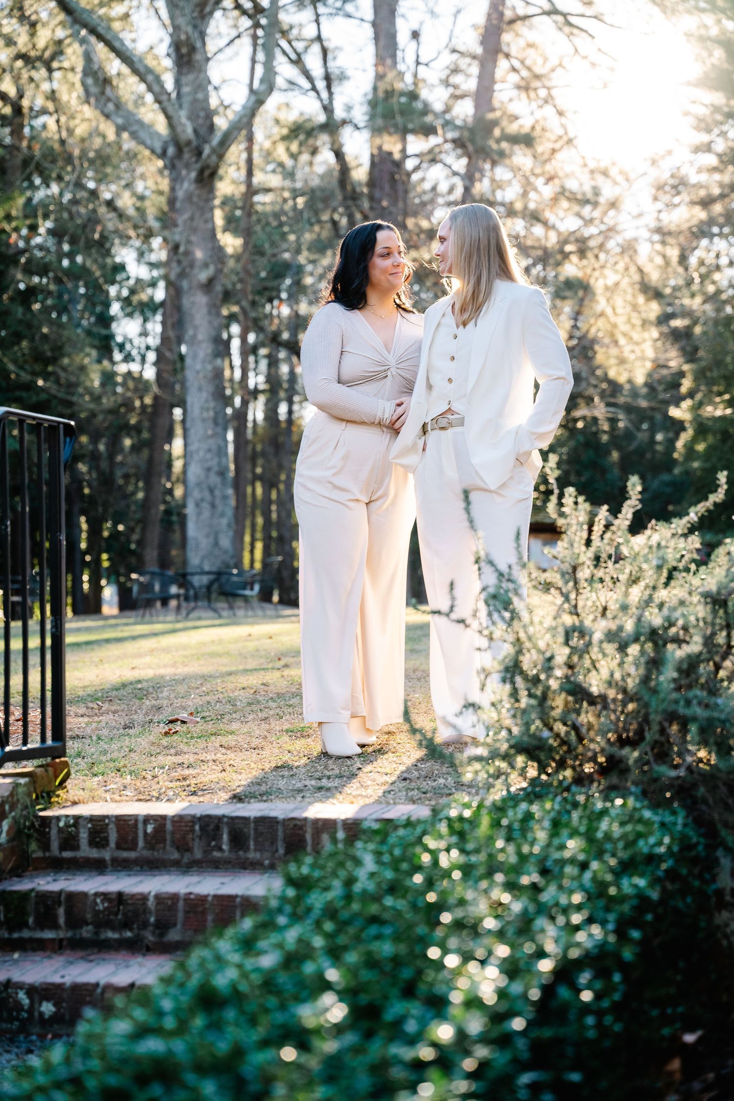 Brides sharing a candid smile against the beautiful, golden-lit scenery of Weymouth Center for Arts and humanities in Southern Pines, NC.
