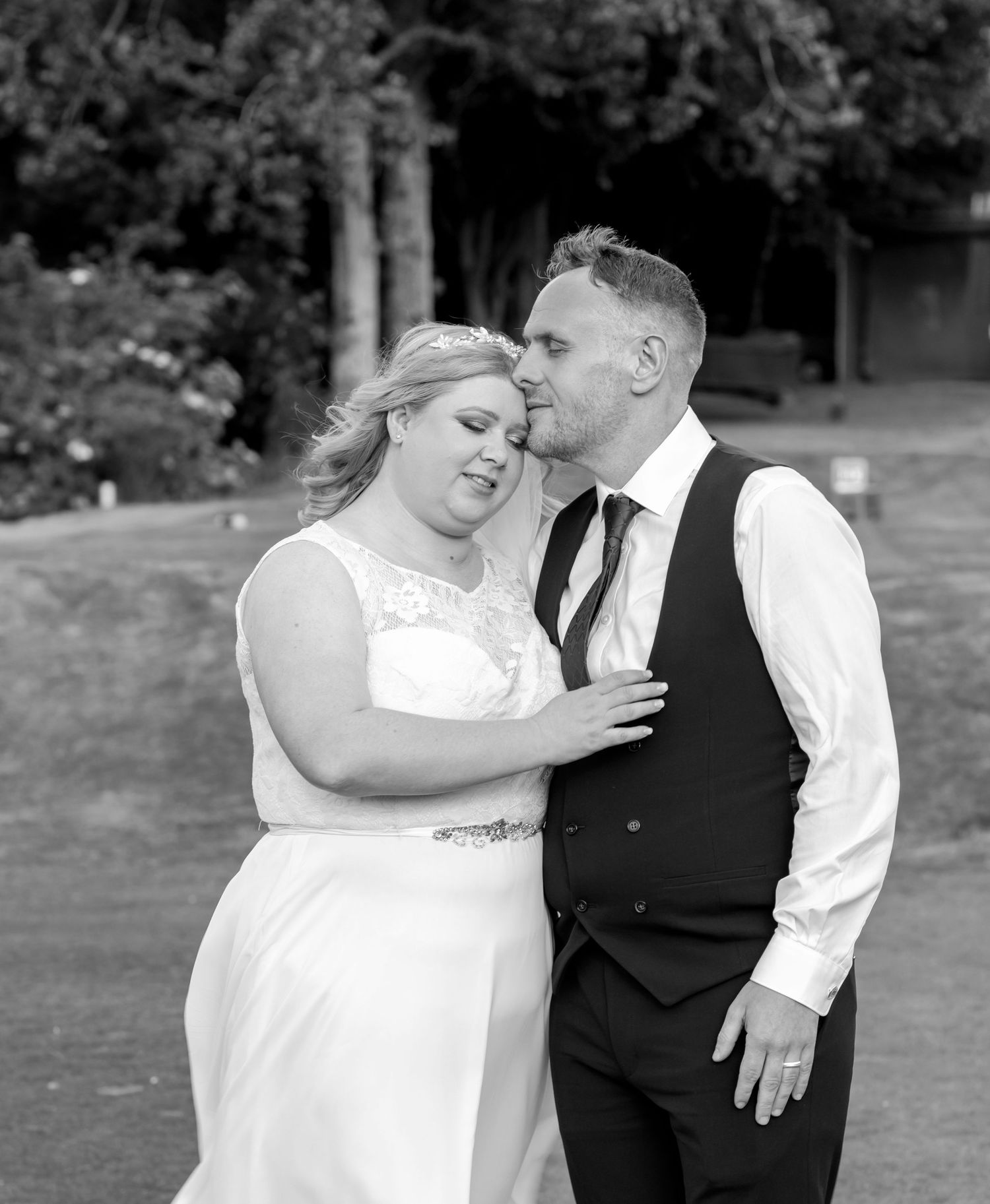 Loving couple embracing on green lawn during outdoor wedding photoshoot.