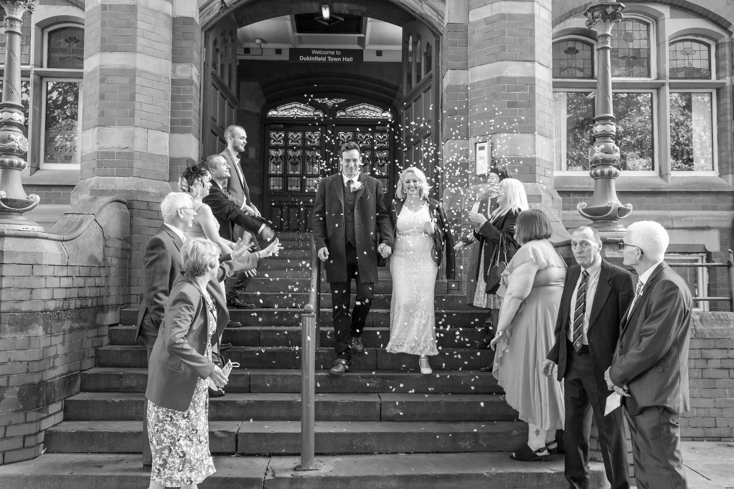 Wedding celebration with guests throwing confetti outside a historic brick church building.