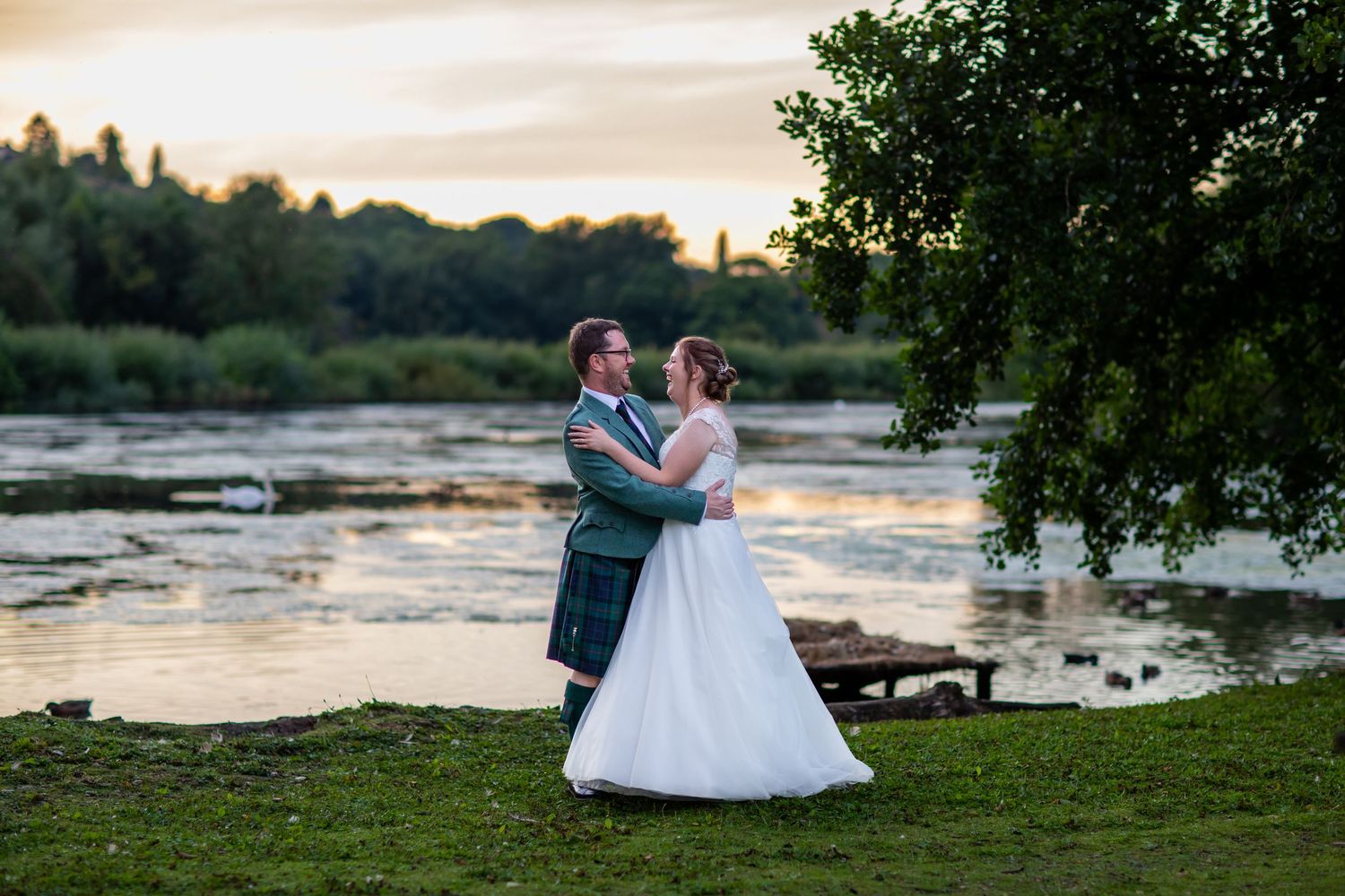 Romantic sunset wedding photos taken along a waterfront with trees in the background.