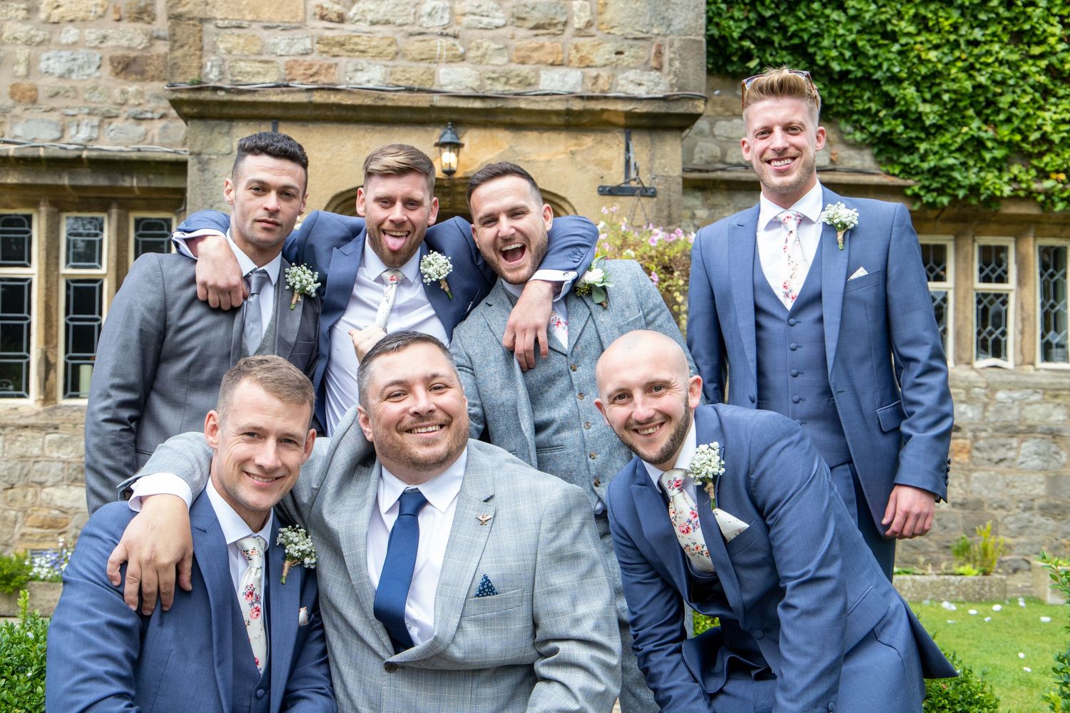Groomsmen in blue suits pose together for group photo outside stone building.
