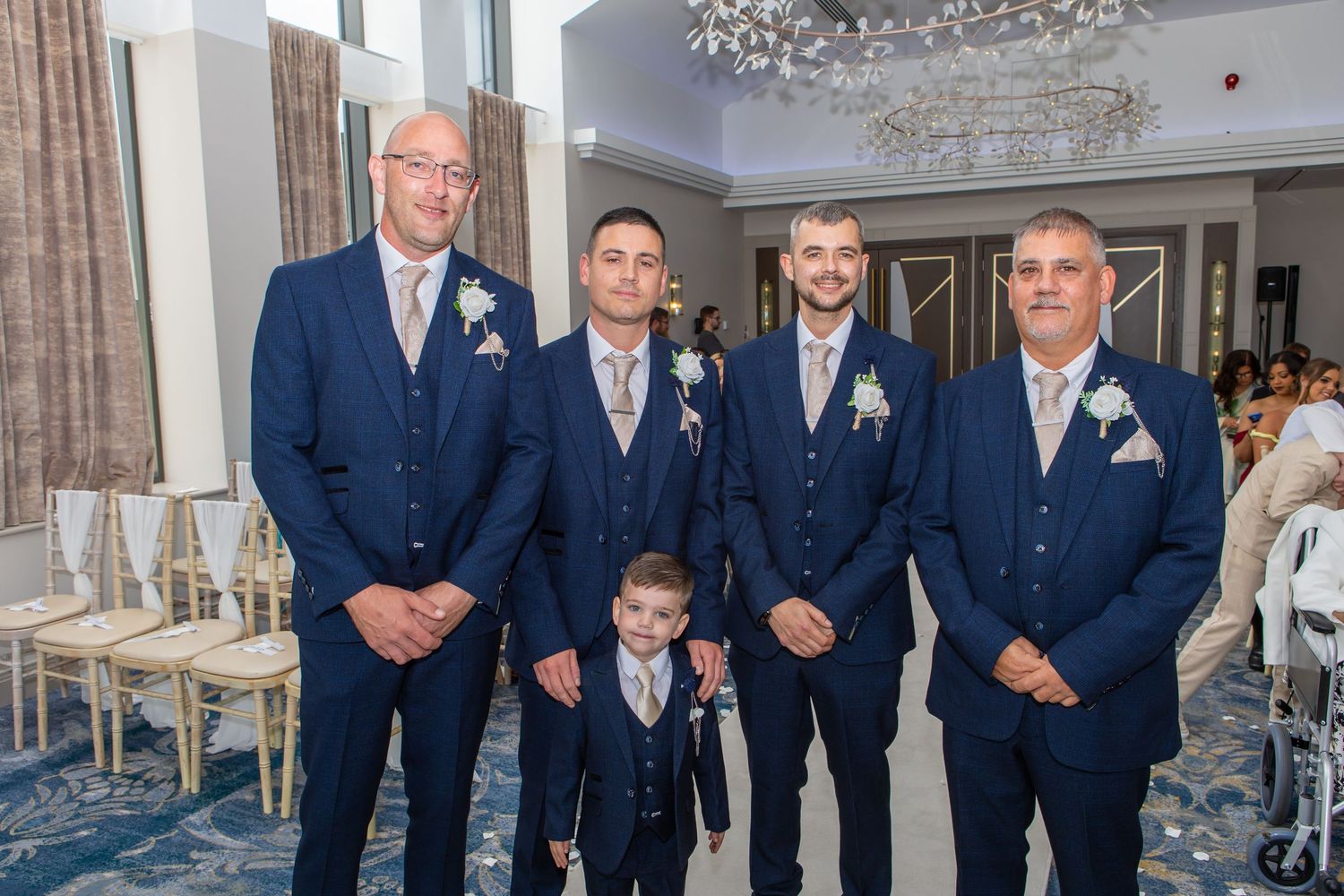 Wedding party members in matching navy suits pose together in an elegant venue during a celebration.