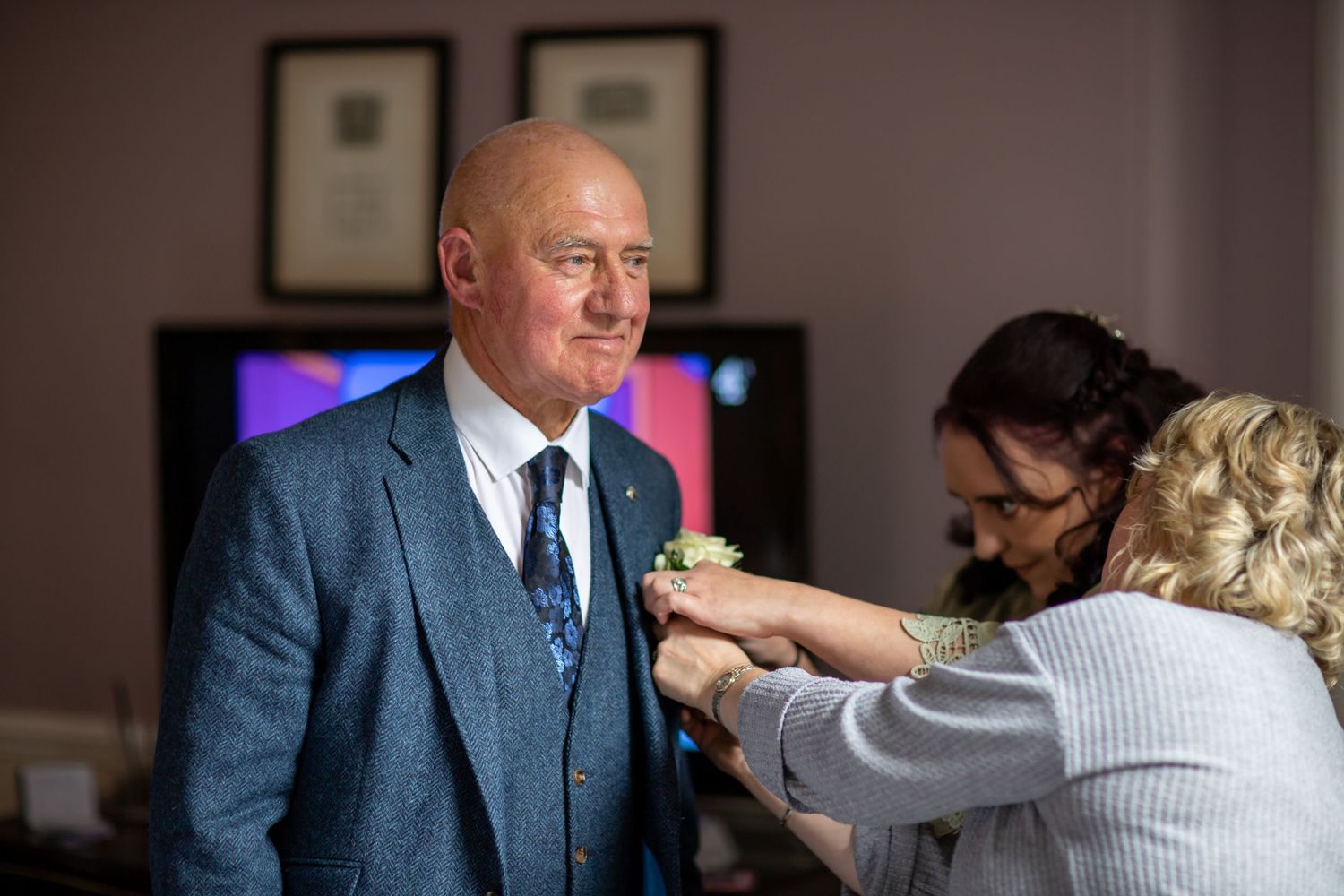 Someone having a boutonniere pinned to their blue three-piece suit jacket during a formal event.