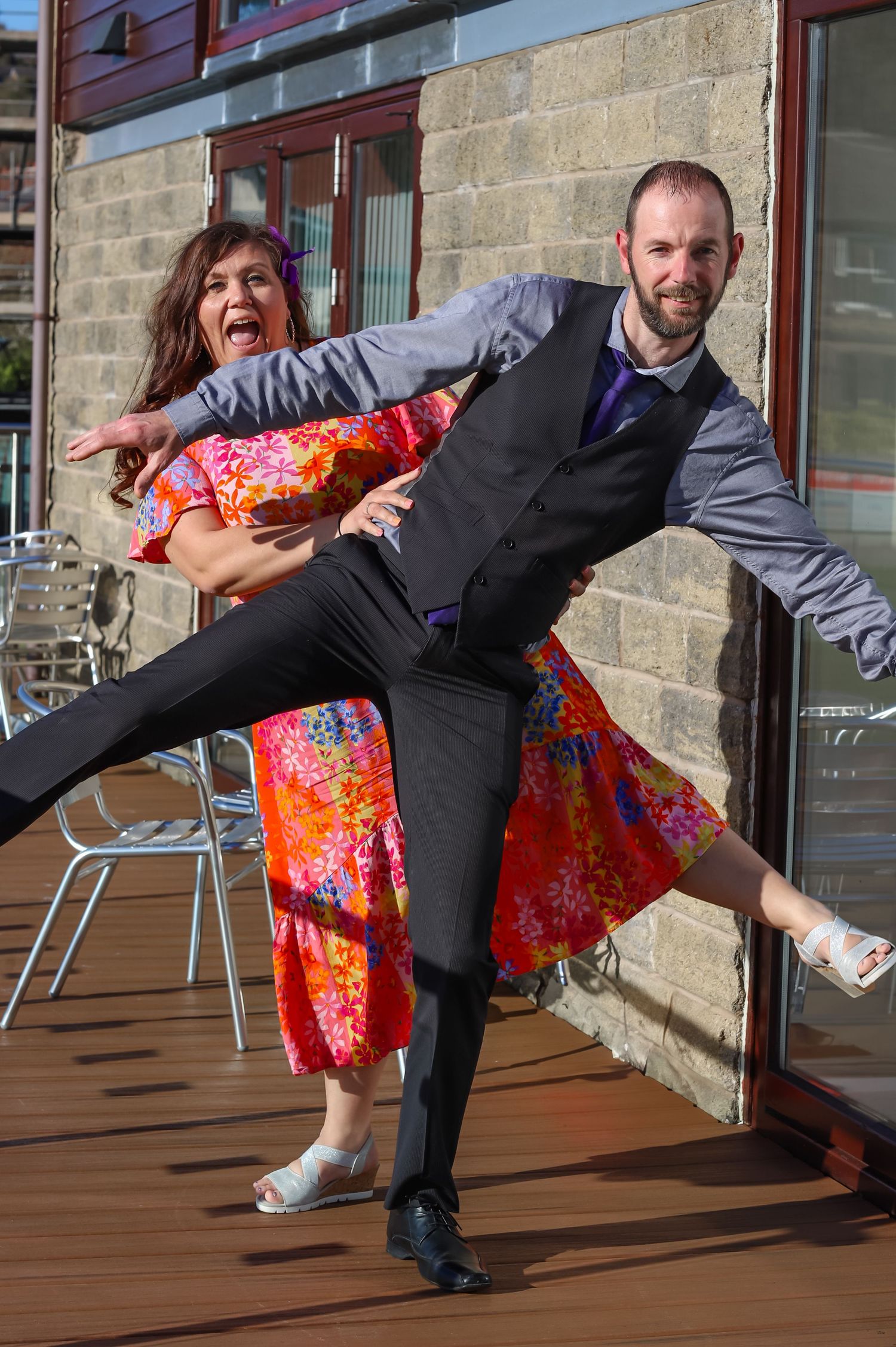 Wedding guests strike playful dance pose on outdoor deck.